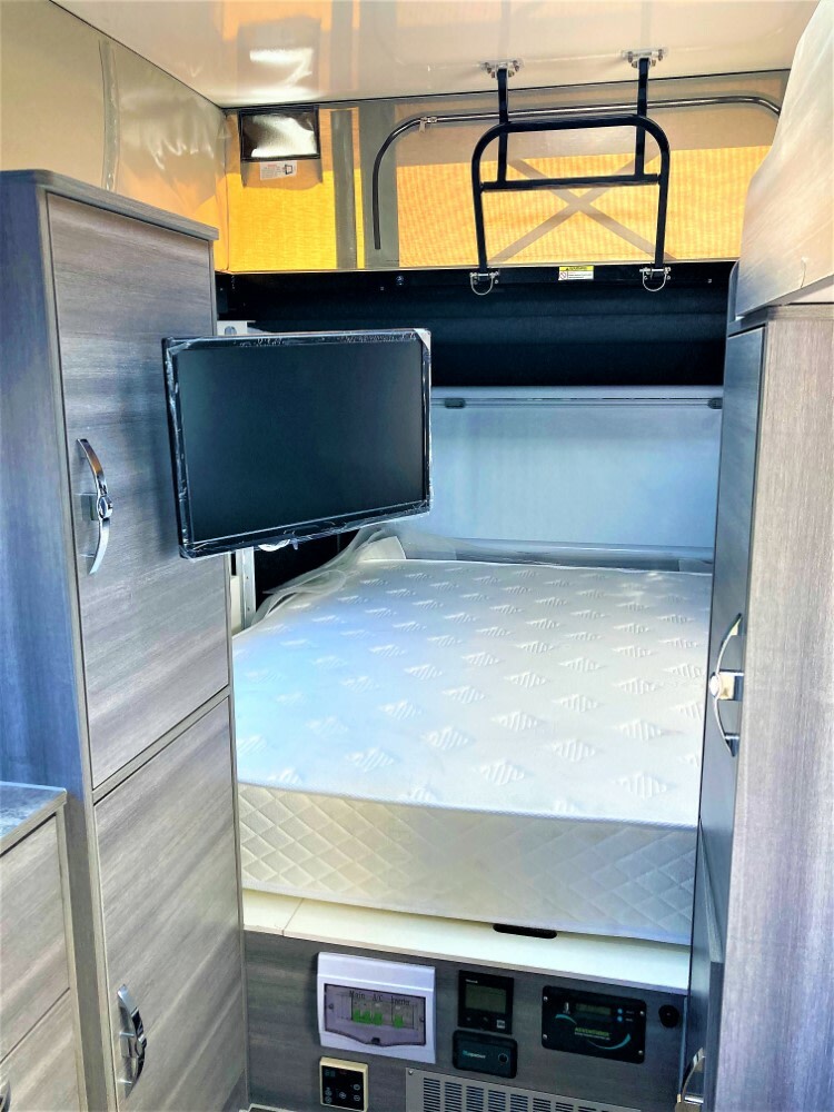 Interior of an RV rental showing a compact bedroom with a bed, wall-mounted TV, cabinets, & control panels.. OBI OBI Popup Trailer 2022