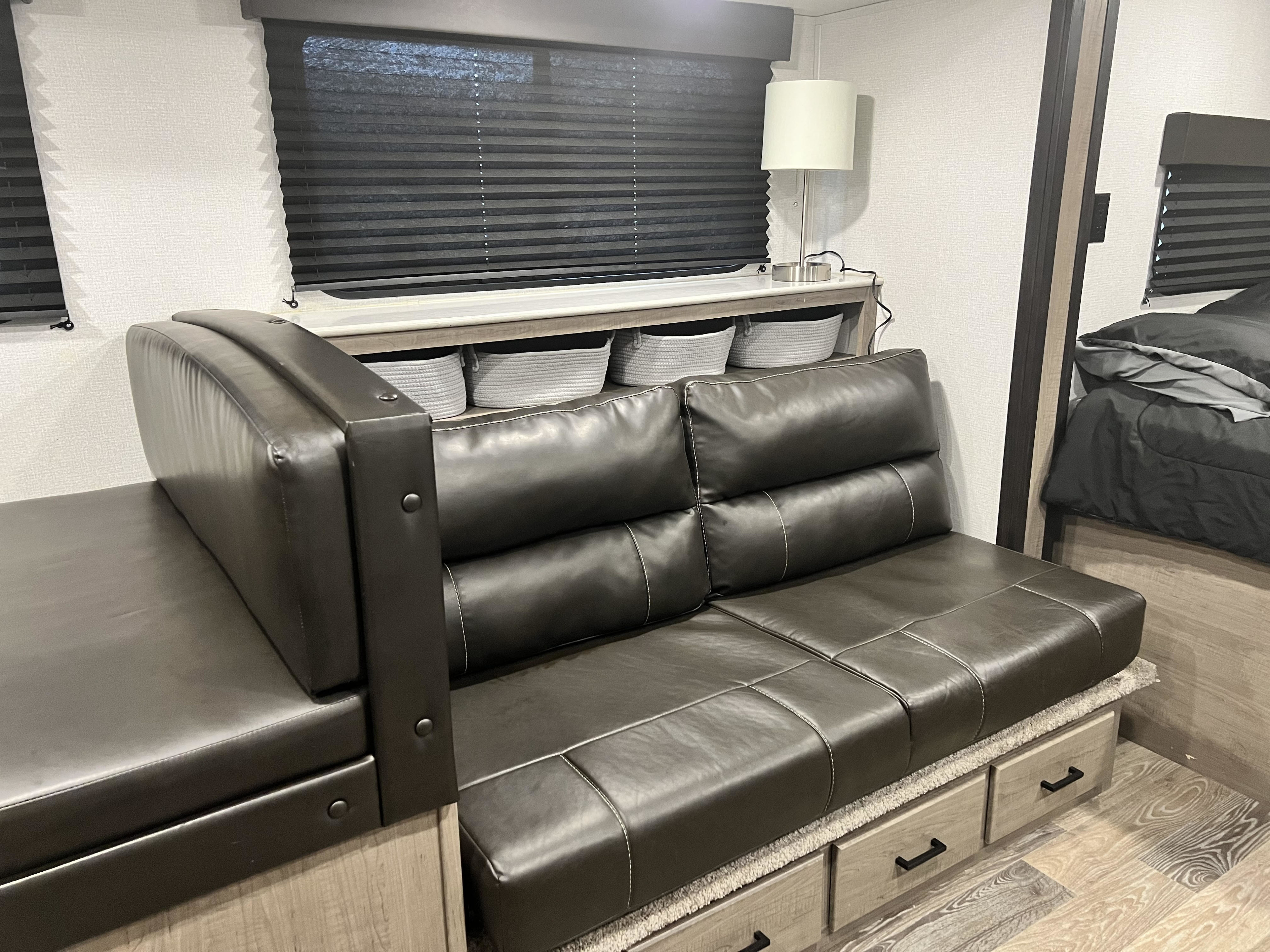 Spacious RV rental interior: L-shaped leather seating with storage drawers, lamp, and blinds for a comfy stay.. Keystone RV Hideout 2021