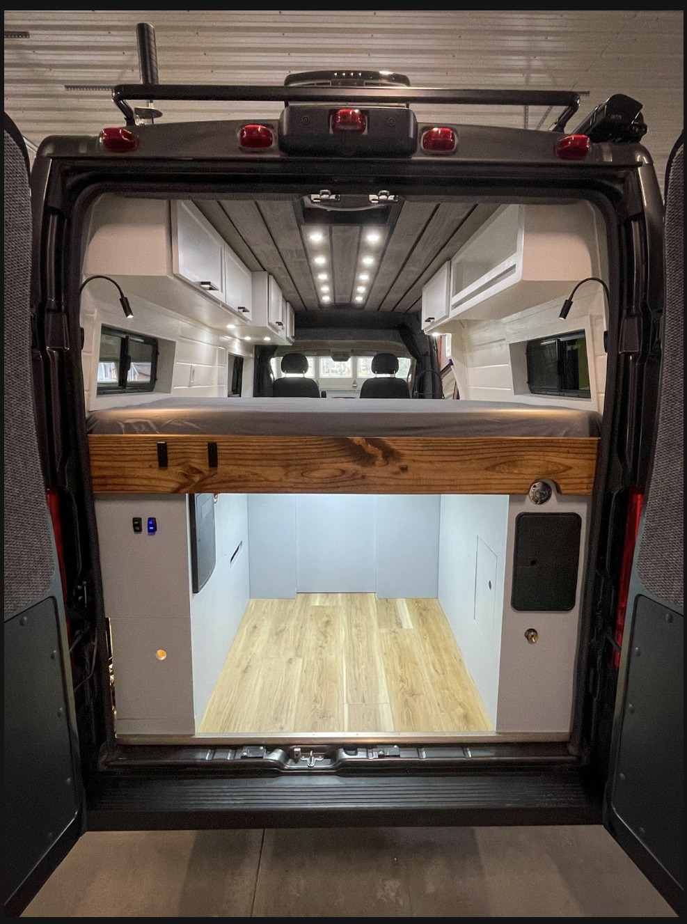 Inside an RV rental, this custom camper van features an elevated bed, overhead cabinets, and large rear storage space.. Ram Promaster 2500 2021