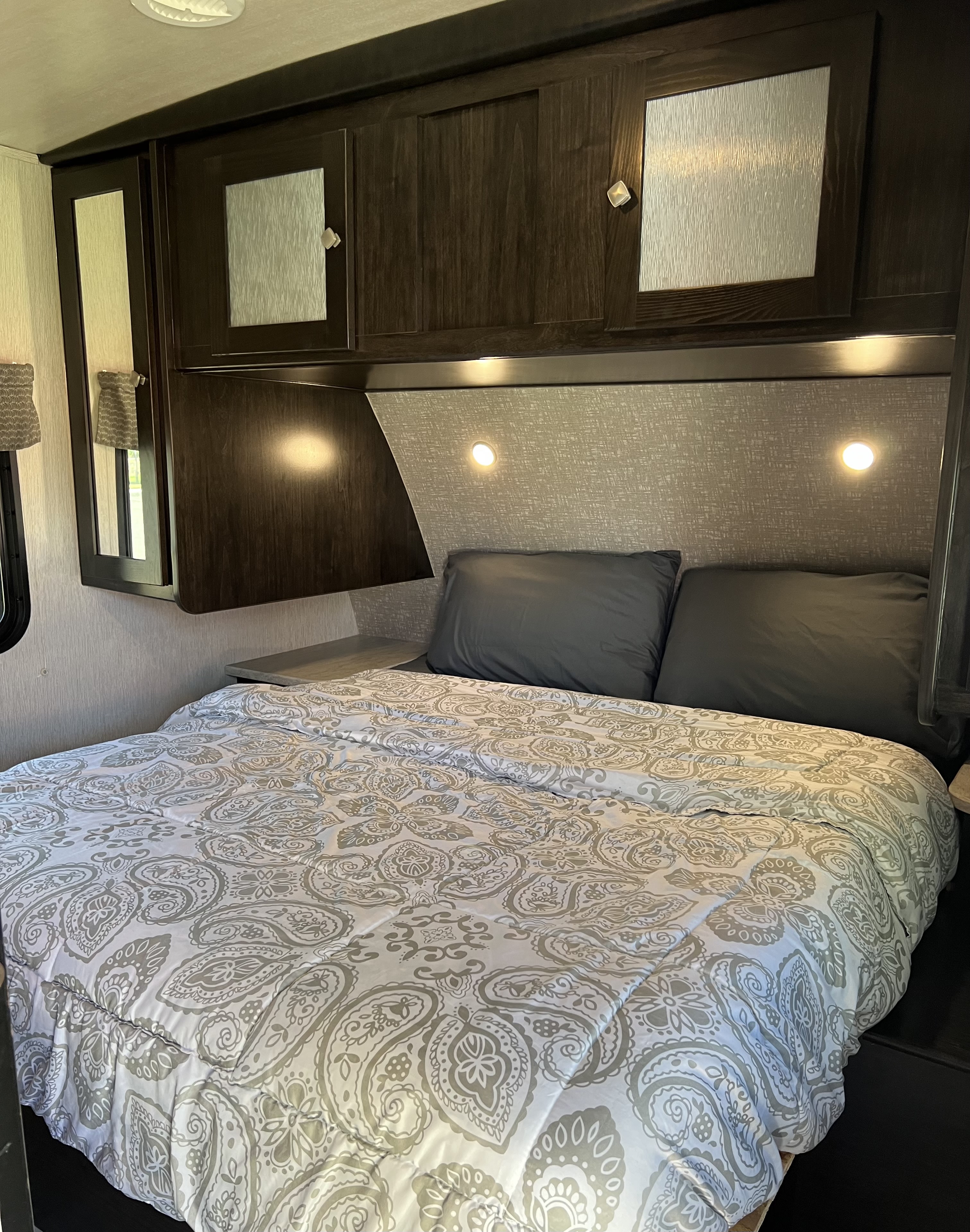 Comfortable RV rental bedroom with a grey paisley comforter, dark cabinets, and integrated reading lights. A cozy travel space.. Heartland RVs North Trail 2018