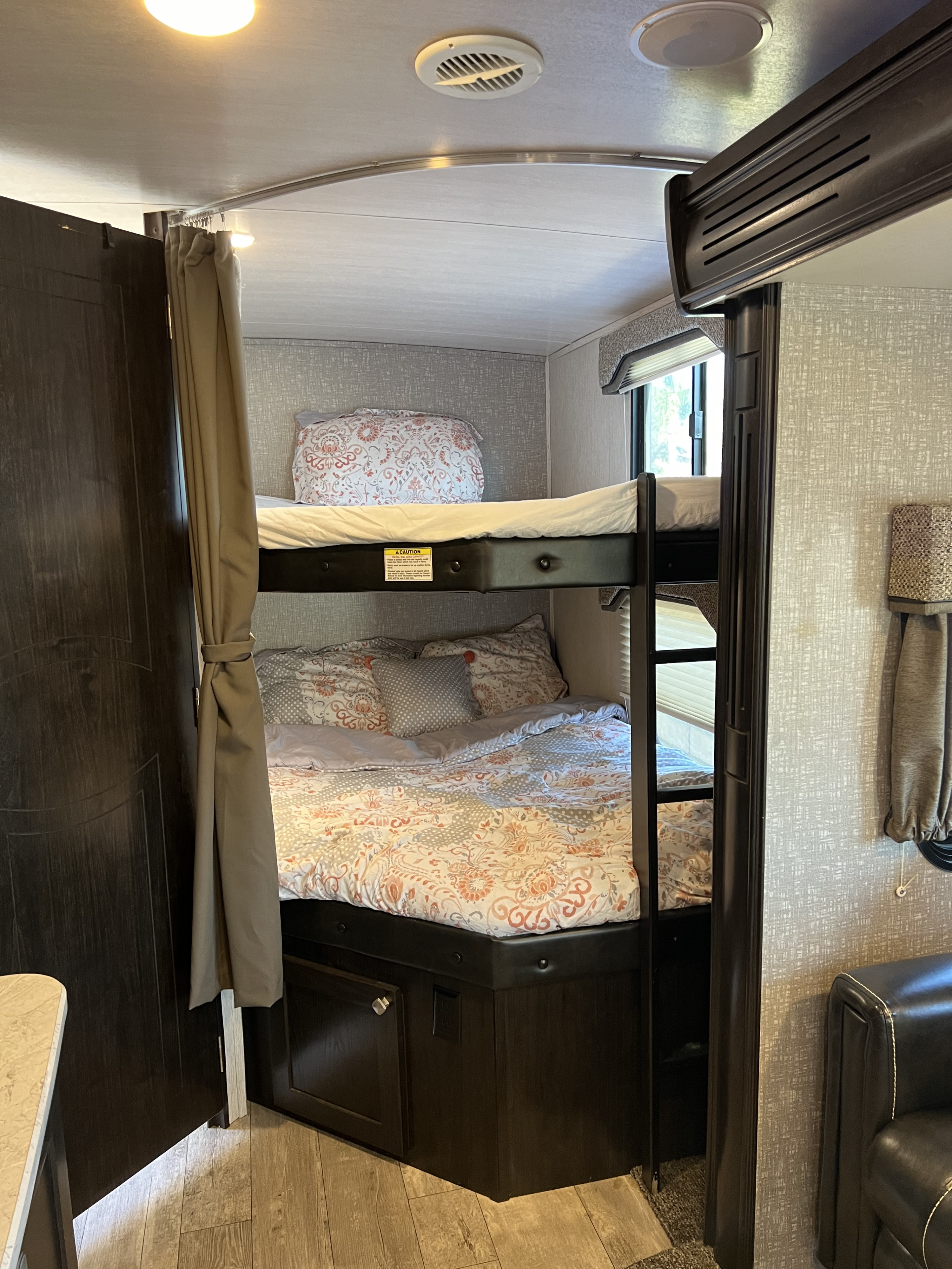 RV rental bunk beds: a cozy interior with patterned bedding, privacy curtain, and dark wood cabinetry.. Heartland RVs North Trail 2018