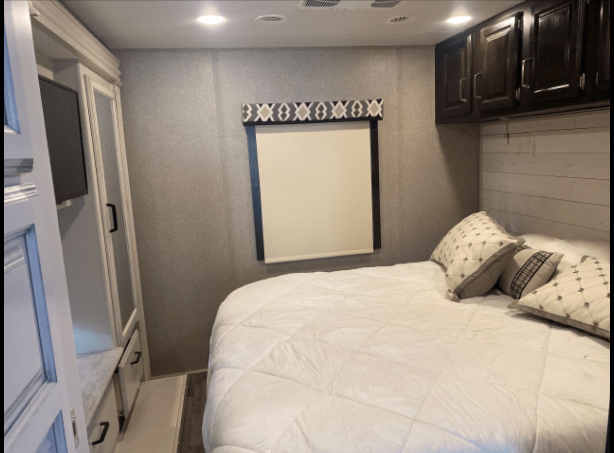 This cozy RV rental bedroom features a comfy bed, overhead cabinets, and a TV, providing comfort on your travels.. Jayco Precept 2021
