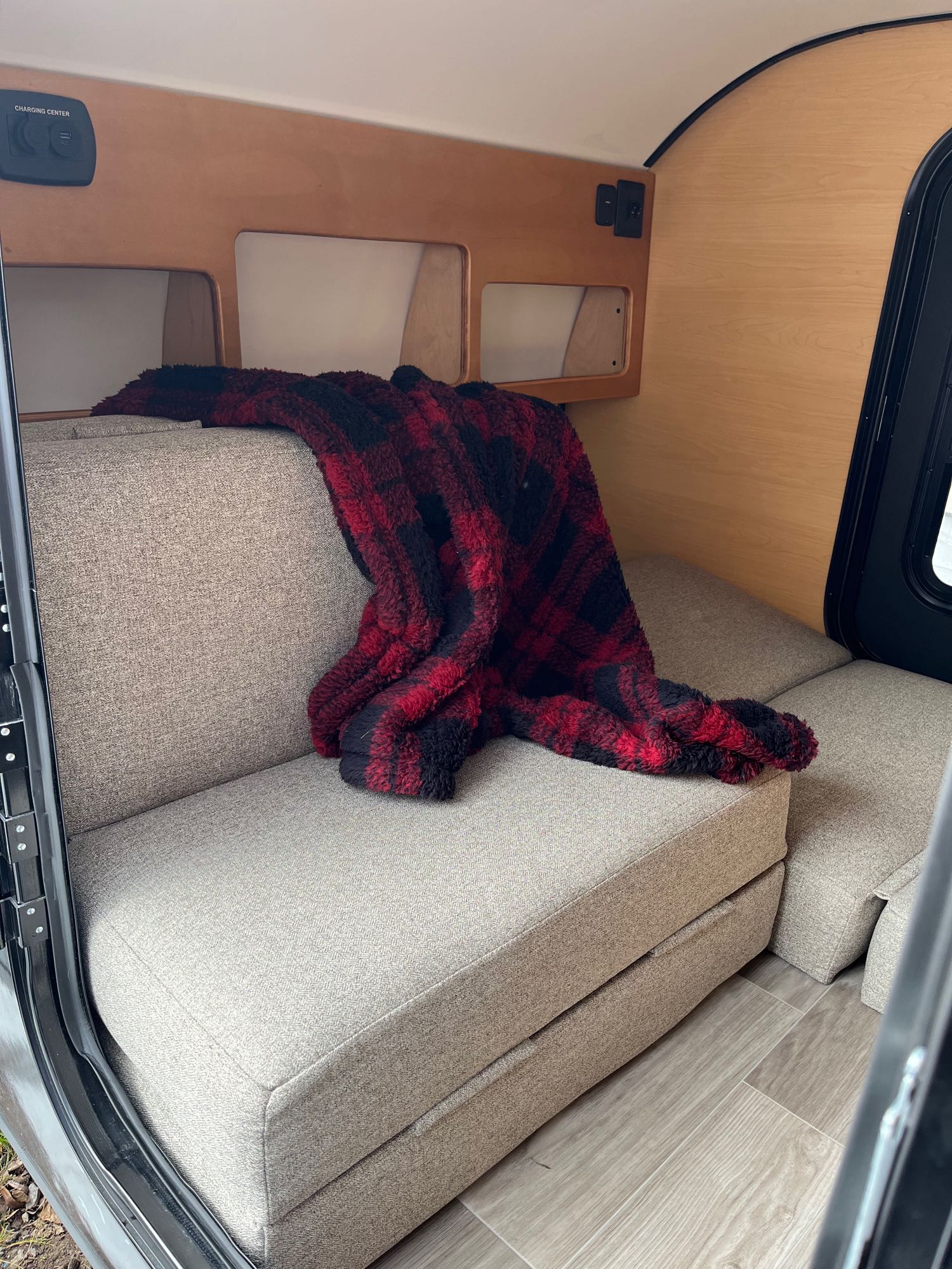 An RV rental interior features light wood walls, comfortable convertible seating with a plaid blanket, and a convenient charging center.. Modern Buggy Little Modern Buggy 10RK 2024