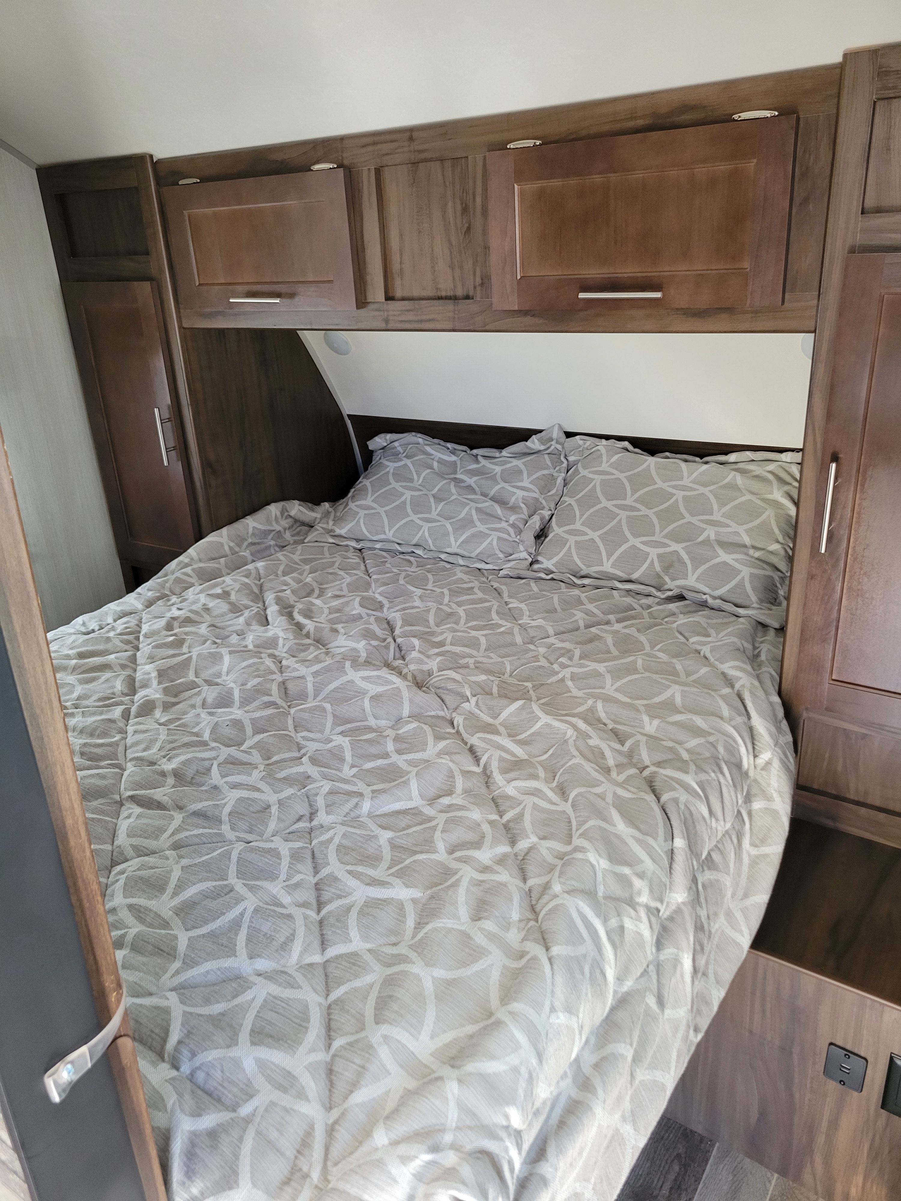 Cozy RV rental bedroom with patterned bed, pillows, and ample wood-toned storage cabinets.. Forest River Cherokee Grey Wolf 2019