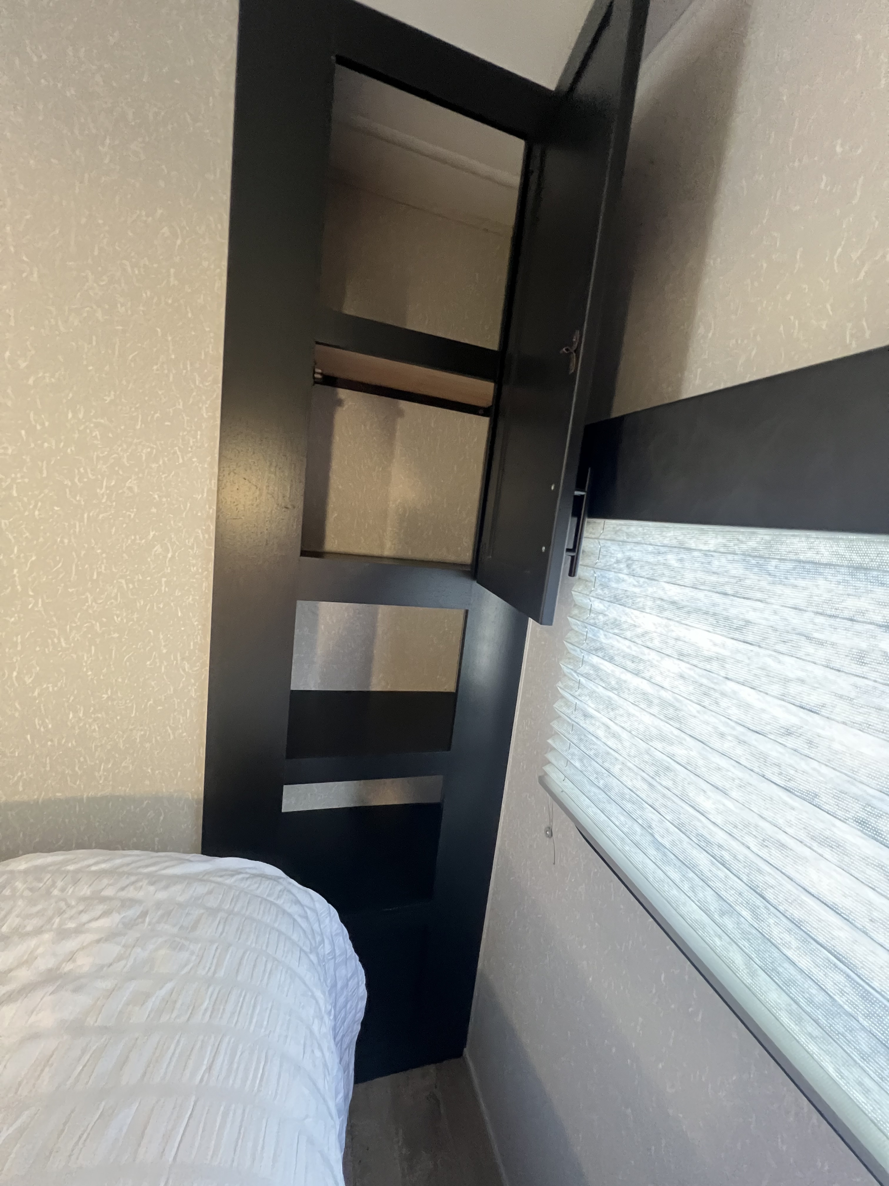 RV rental bedroom featuring an open storage cabinet with shelves, a cozy bed, and window with privacy blinds.. Forest River Cherokee 2022