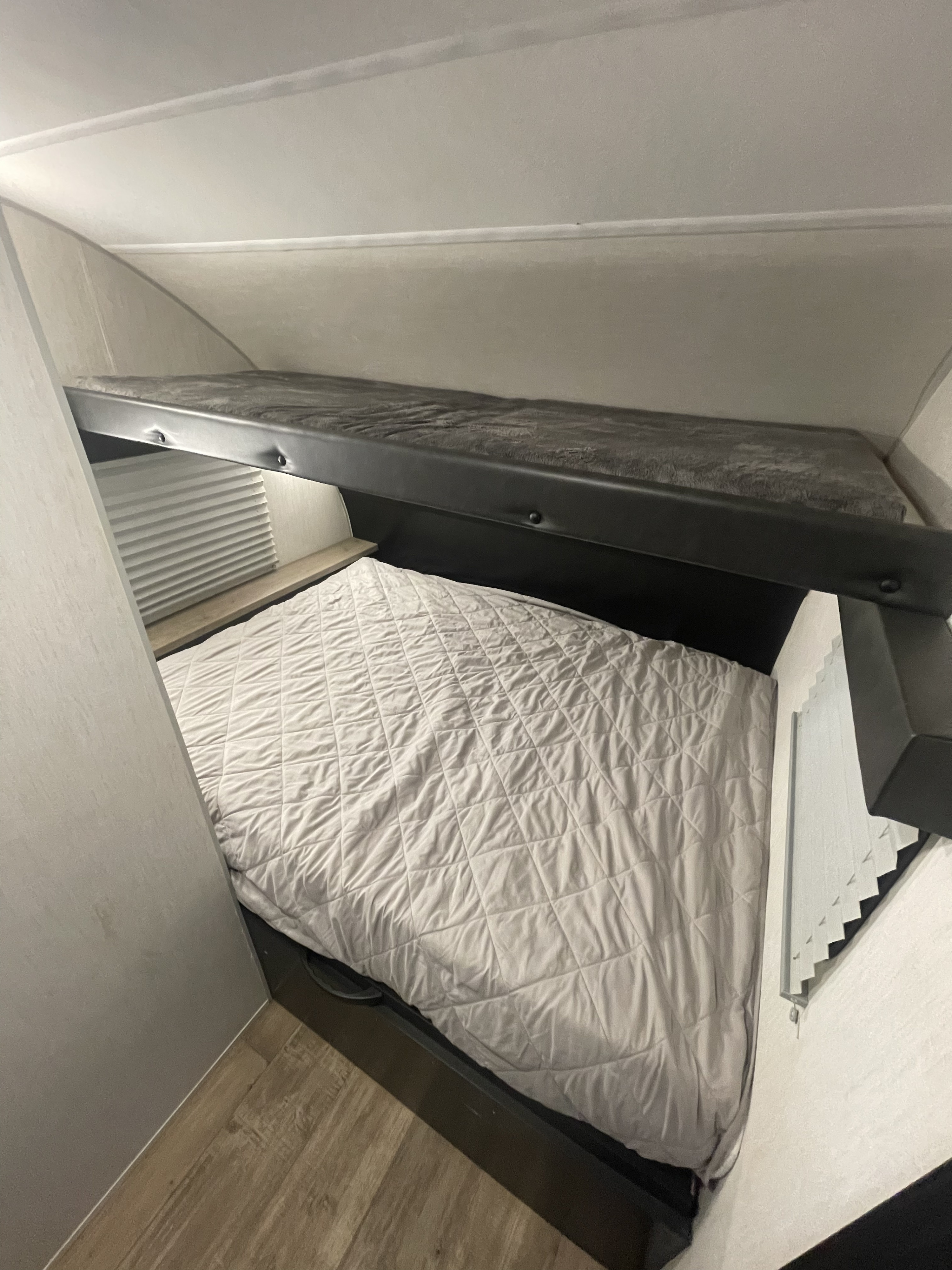 Inside an RV rental, showing a well-made lower bunk with a quilted comforter and an upper bunk with a fuzzy blanket.. Forest River Wolf Pup 2022