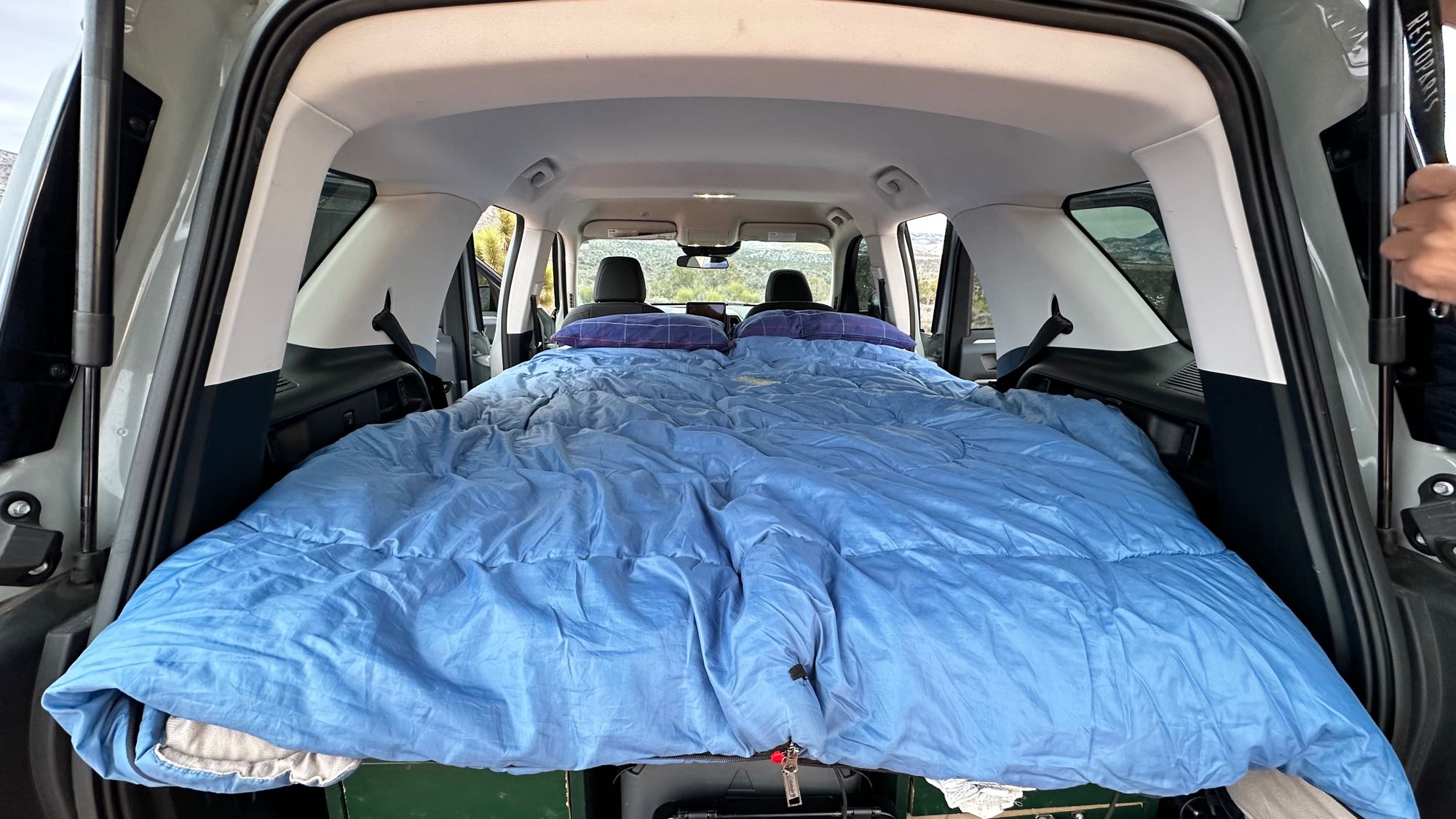 Vehicle's spacious rear transformed into a bed with blue bedding, ideal for an RV rental or car camping adventure.. Ford Bronco Sport 2022