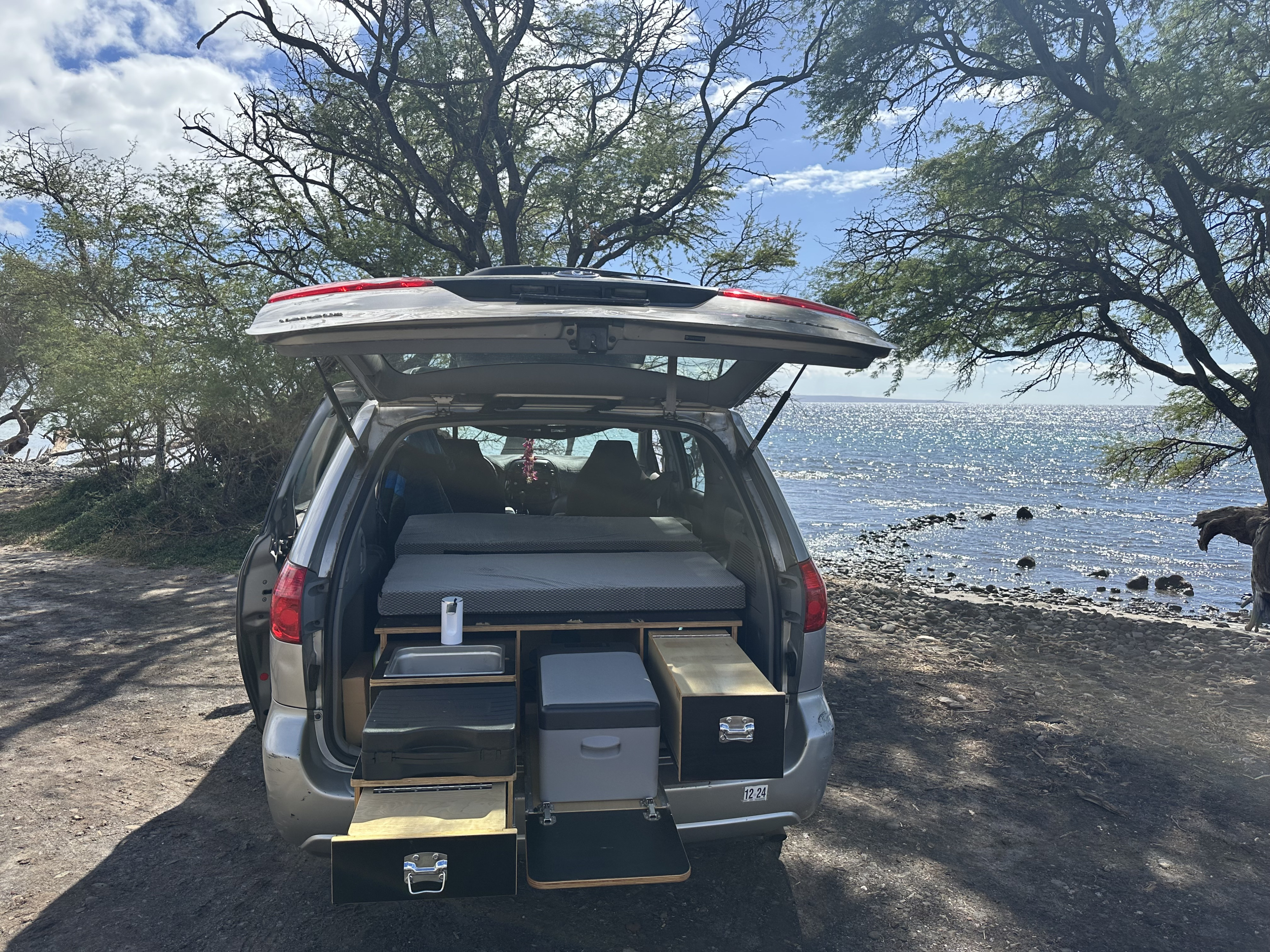 Gray SUV RV rental by the ocean, showing its rear converted into a camper with a bed, sink, and cooler drawers.. Toyota Other 2006