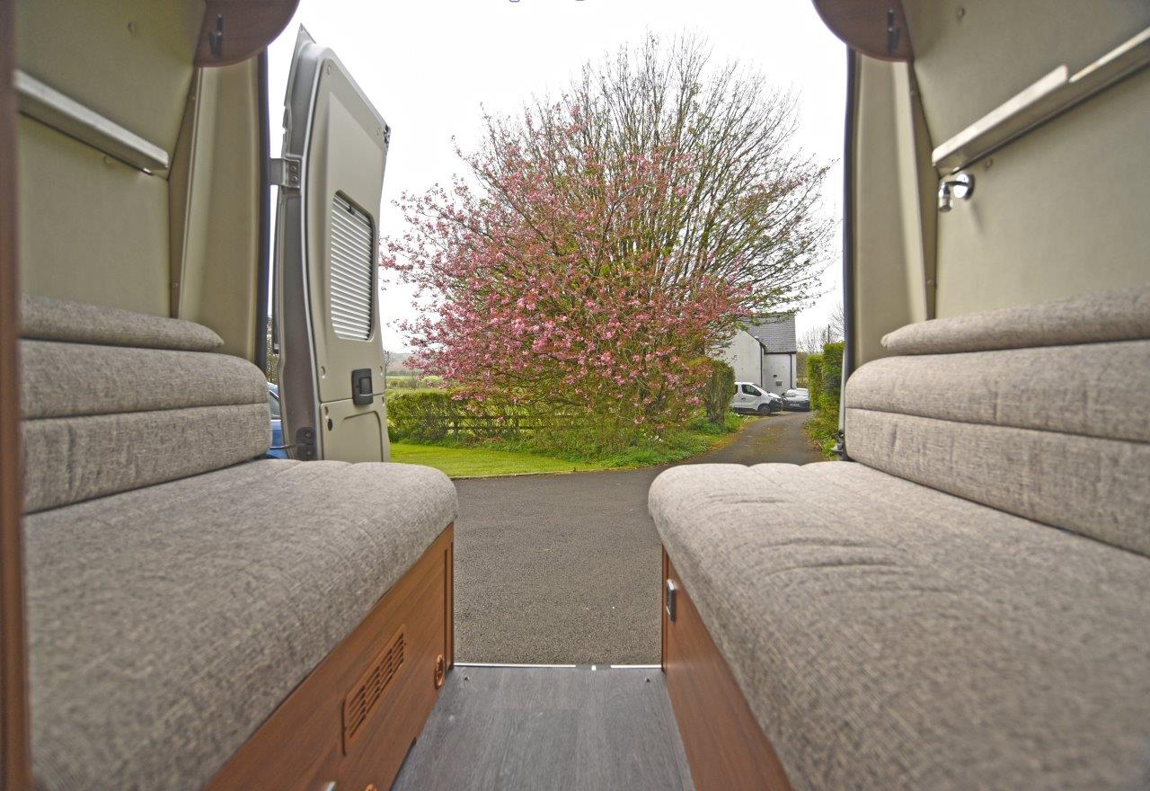 RV rental interior with comfy benches looking out through open rear doors to a vibrant pink tree and driveway. Perfect camper van escape.. Fiat Ducato 2020