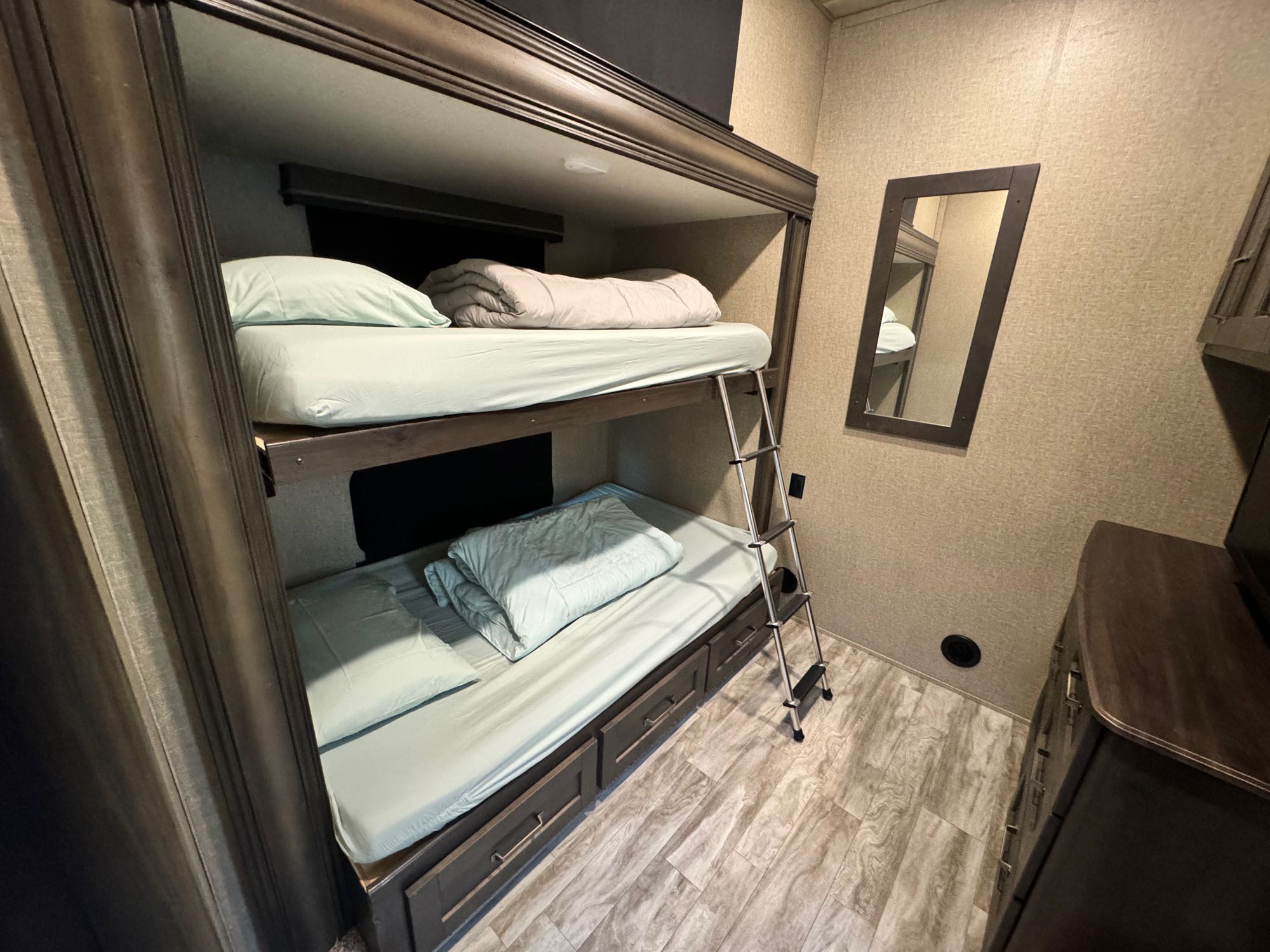 Cozy RV rental bunk beds with light blue bedding, a ladder, and storage drawers below, perfect for family travel.. Grand Design Reflection 2022