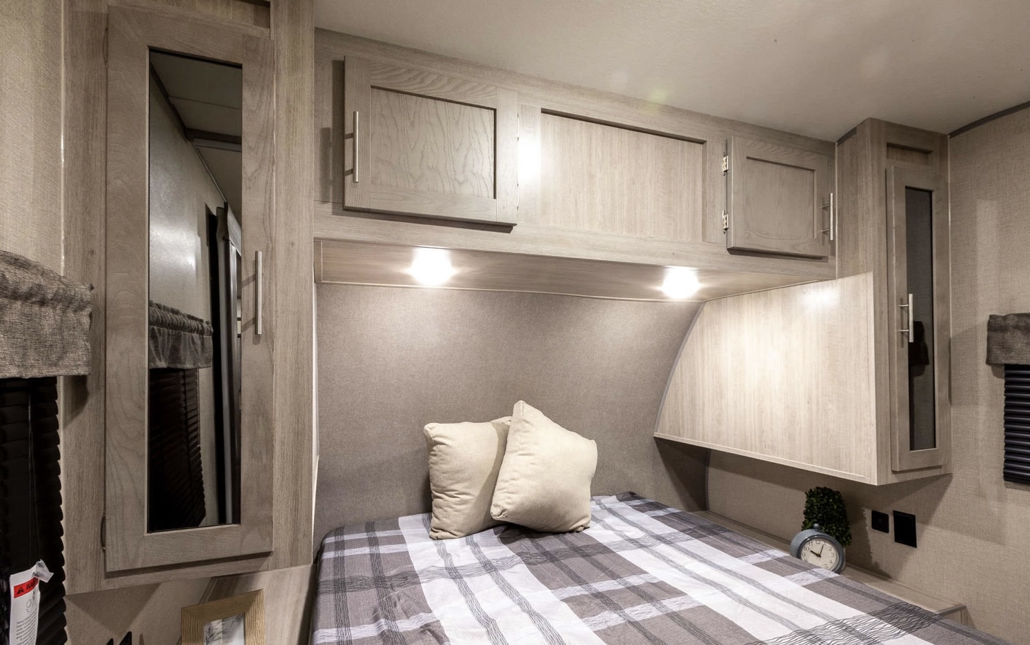 This comfortable RV rental bedroom features a bed with plaid comforter, overhead lights, and ample storage cabinets.. Coachmen Catalina 2022