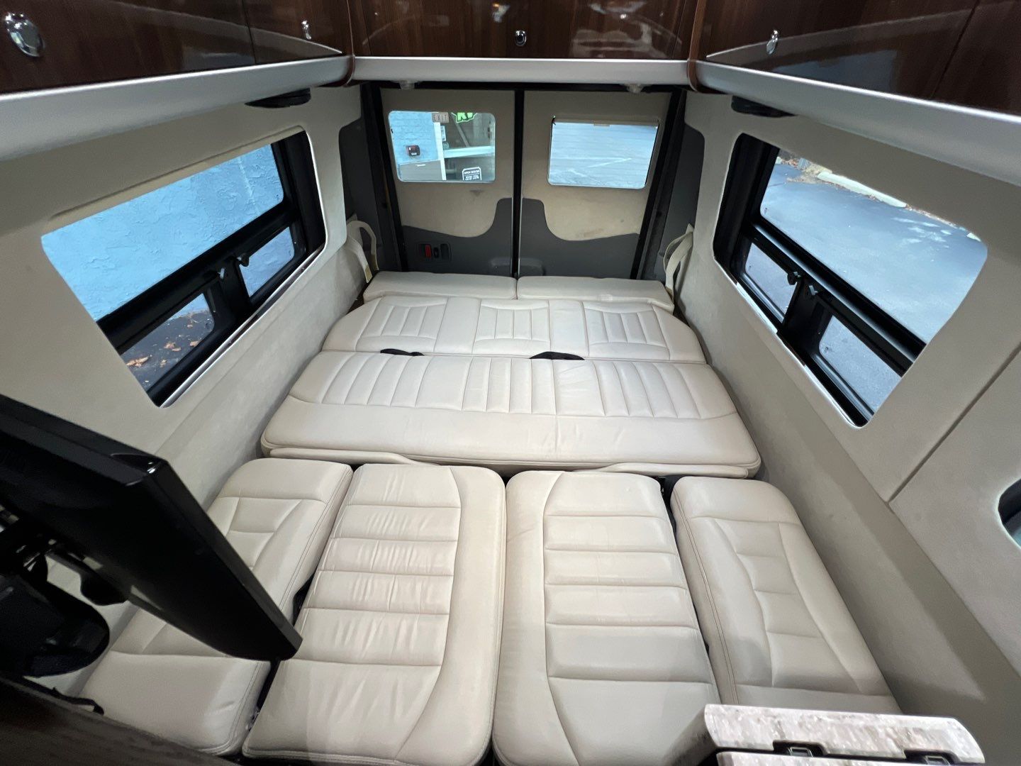 Spacious RV rental interior: cream padded seating laid out to form a bed, with windows & wood cabinets visible.. Airstream Interstate 2016