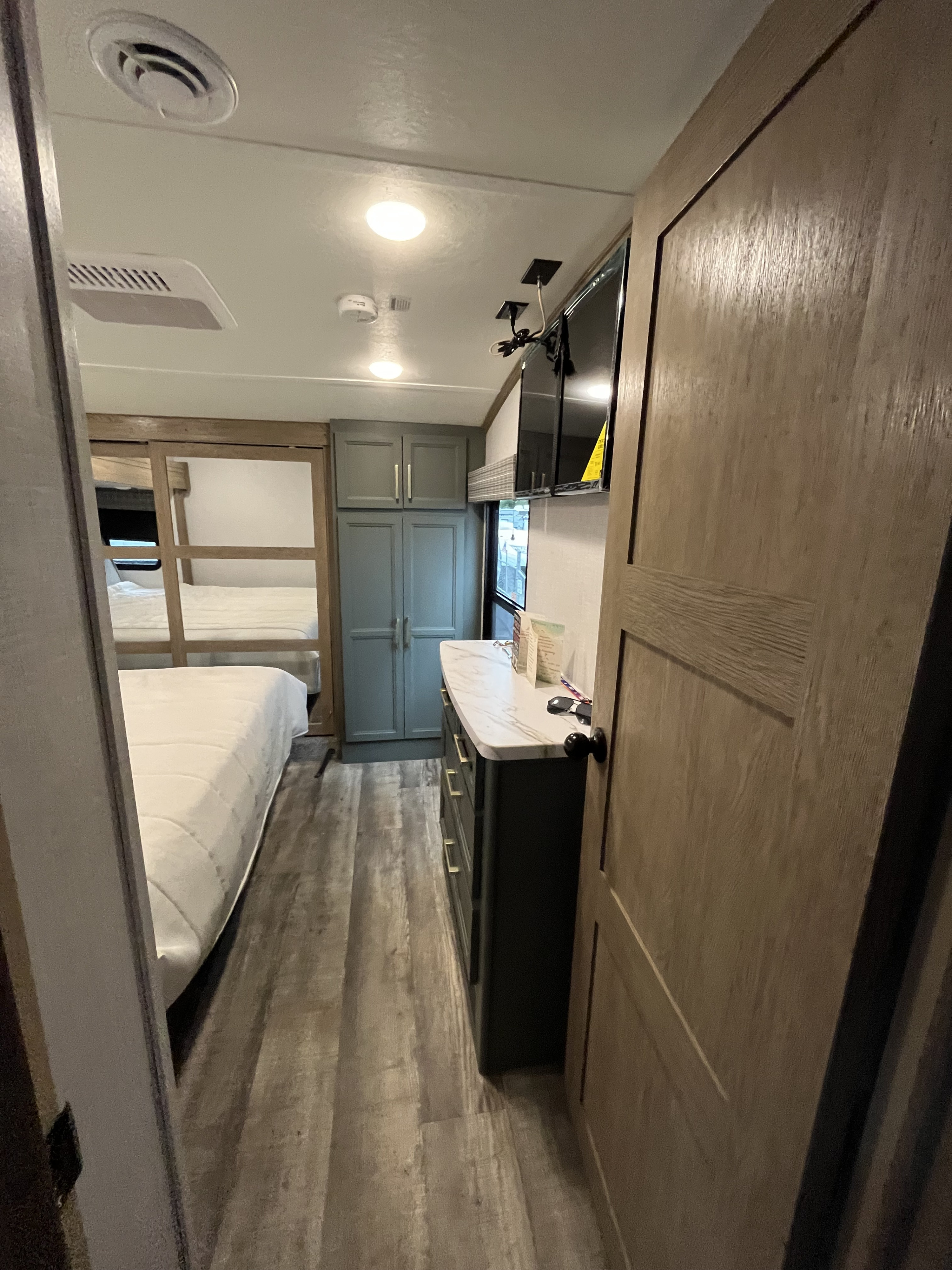 Inside an RV rental: a compact yet comfortable bedroom area with a bed, dresser, mounted TV, and built-in storage.. Dutchmen Eddie Bauer 2023