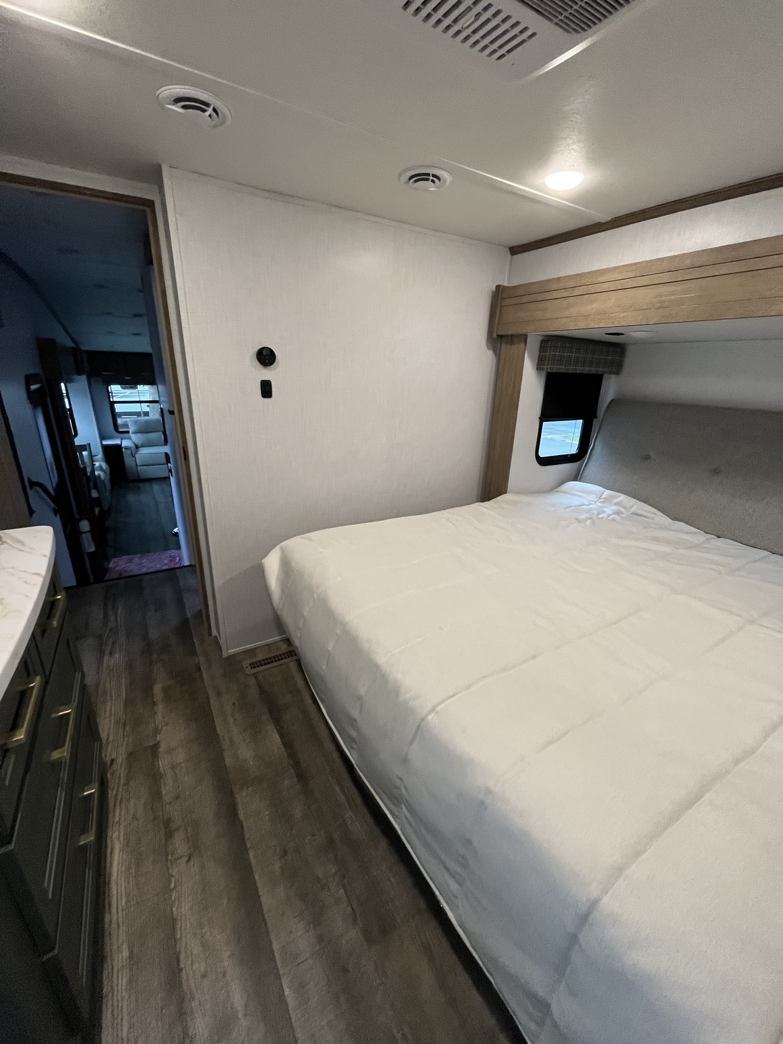 RV rental bedroom showcasing a comfortable bed, overhead lighting, and wood-look flooring, with a glimpse into the living area.. Dutchmen Eddie Bauer 2023
