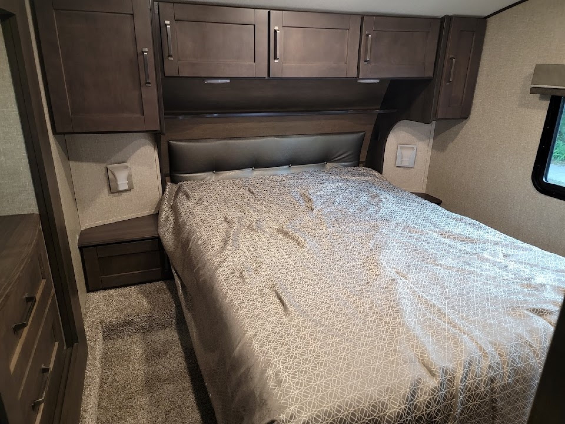 RV rental bedroom: full-size bed with light patterned bedding, dark wood cabinetry, and ambient lighting.. Grand Design Reflection 2020
