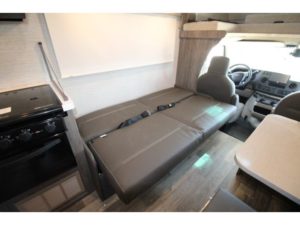 RV rental interior: Compact living space with a dark gray convertible sofa bed, kitchen stovetop, and front cab view.. Winnebago Minnie Winnie 2024