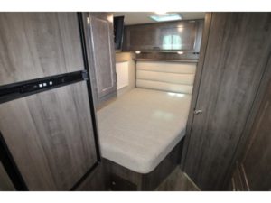 Inside an RV rental: a cozy bedroom featuring a comfortable bed, wood-paneled storage, and a mini-fridge.. Winnebago Minnie Winnie 2024
