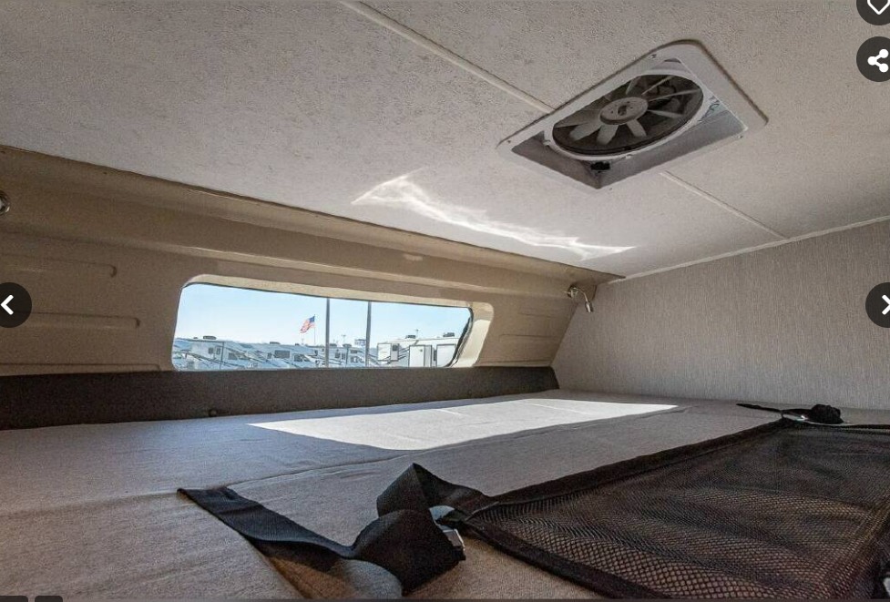 RV rental: Over-cab sleeping area with a large bed, window showing other RVs & flag, ceiling fan, and storage net.. Coachmen Leprechaun Premier 2023