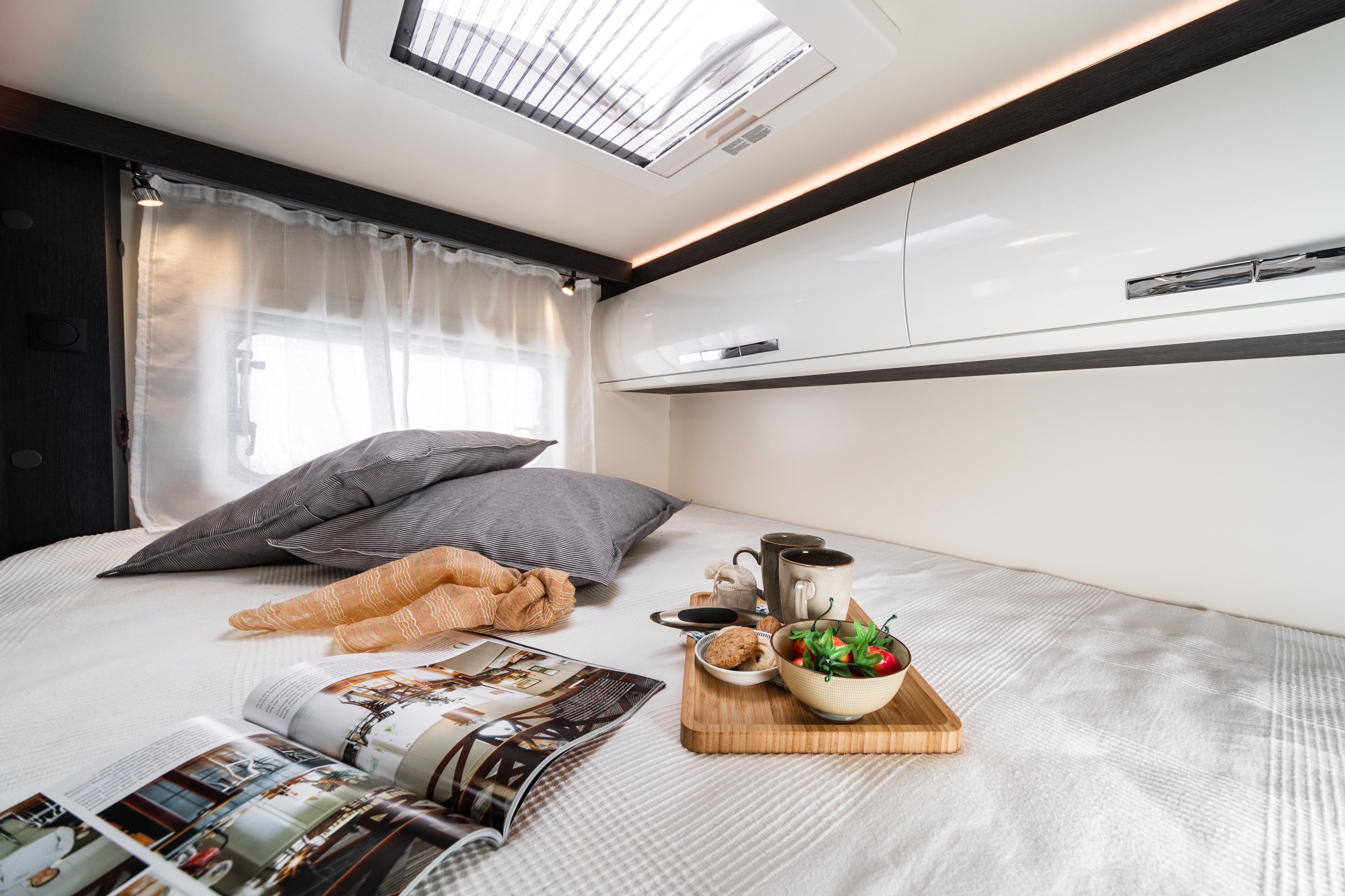 Cozy RV rental bedroom: bed with breakfast tray, magazine, pillows, overhead storage & skylight.. Roller Team Zefrio 665 2021