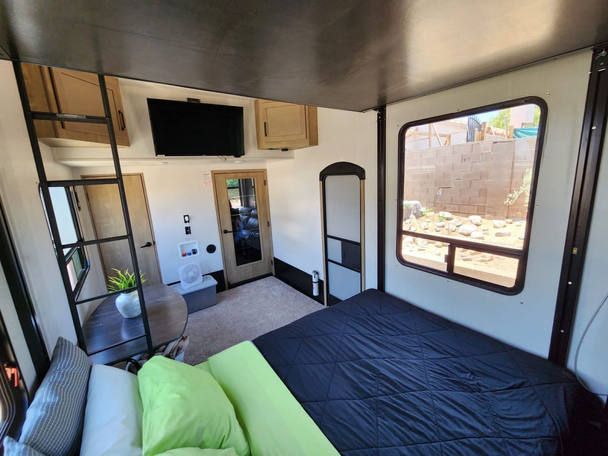 RV rental interior: a comfy bed with lime green accents, TV, bunk ladder, and outdoor view from the window.. Keystone Carbon 2023