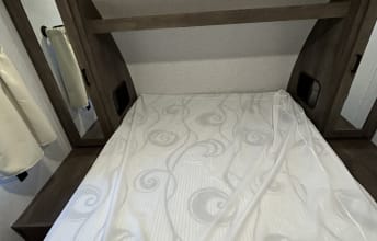 This RV rental shows a compact bedroom. A white, patterned bed is centered with wood shelving/cabinets surrounding it, perfect for travel.. Forest River Salem Cruise Lite 2022