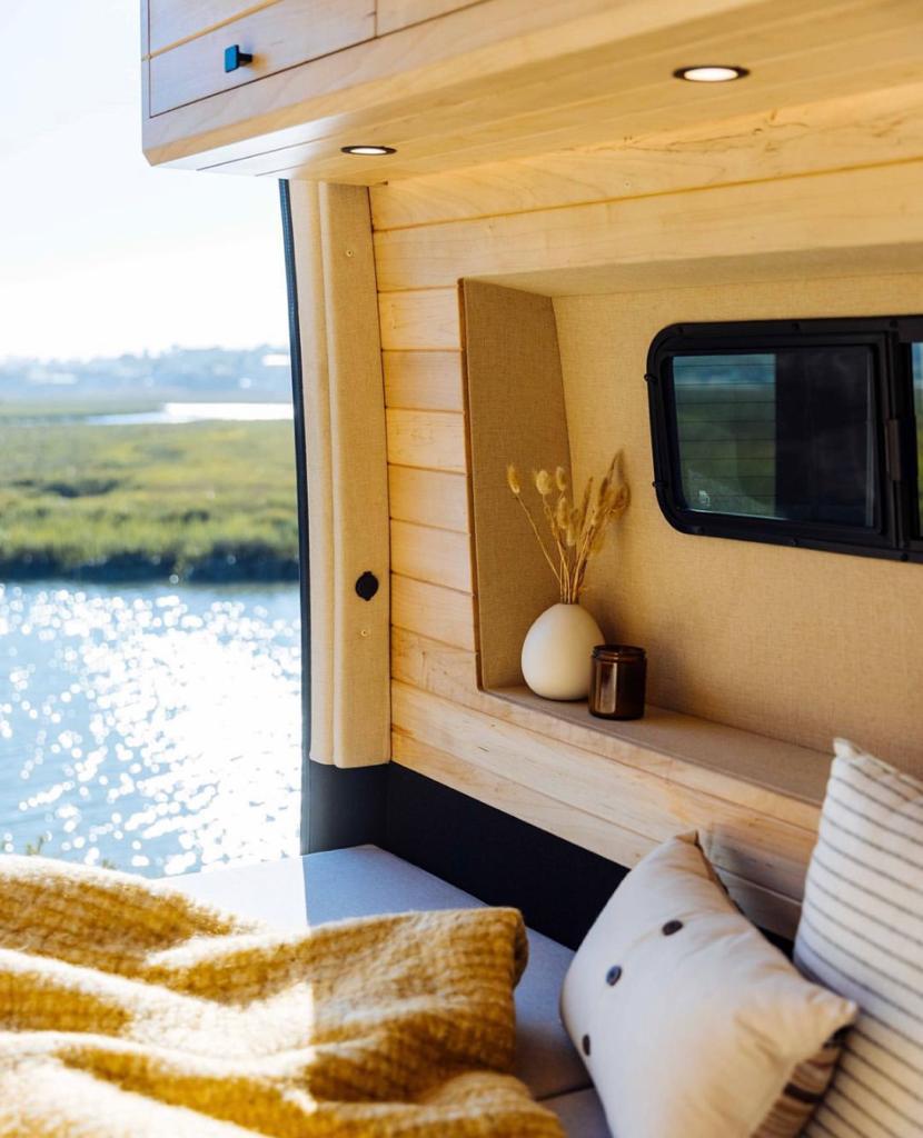 This cozy RV rental offers a modern wood interior, soft seating, and a window view of a sparkling lake.. Vanspeed Mercedes Sprinter 2021