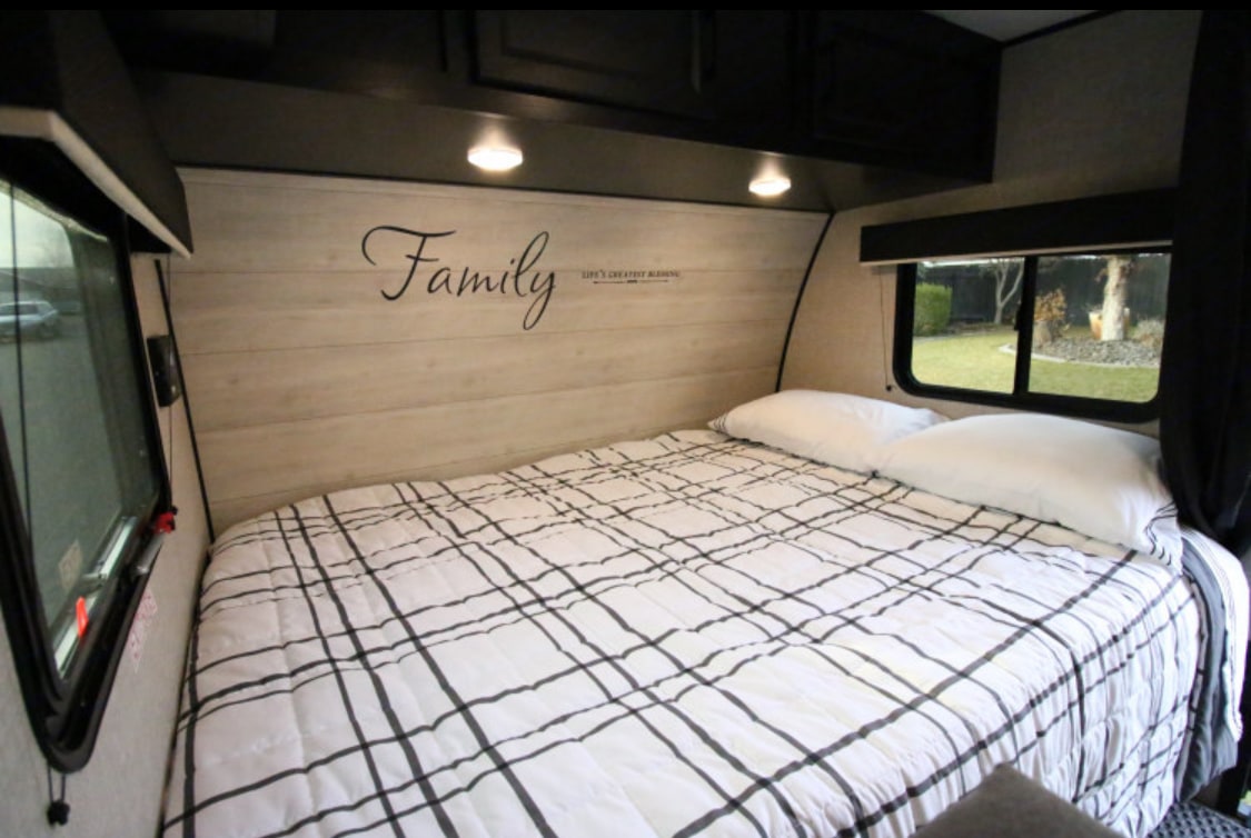 Spacious RV rental bedroom featuring a large bed with white and black plaid bedding, wall decal, and bright windows.. Jayco Jay Flight SLX Baja Edition 2023