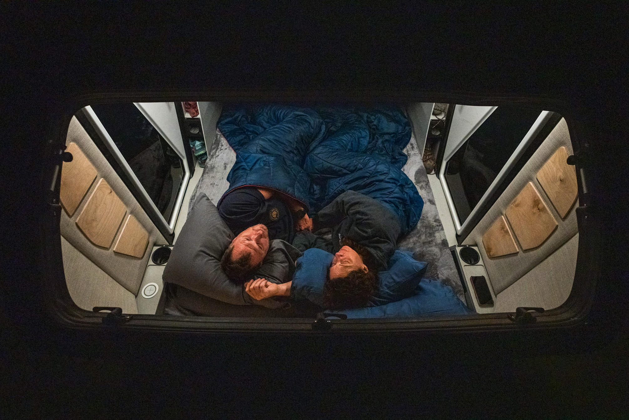 Overhead view: A couple sleeps soundly on a cozy bed inside their RV rental, showcasing the comfortable camper van interior.. Escapod TOPO2 Voyager 2024