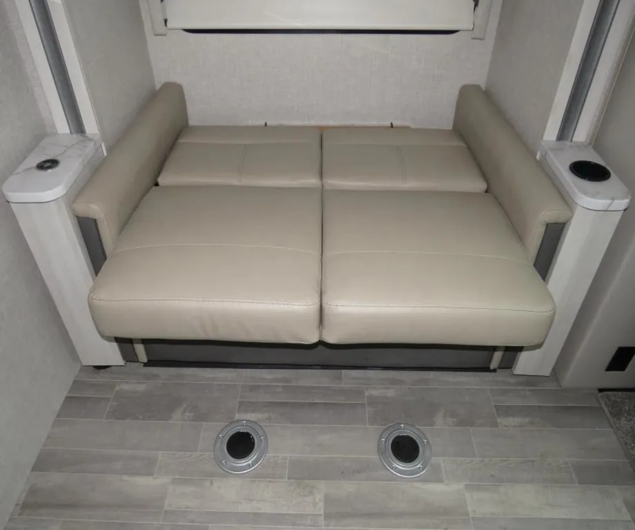 RV rental: Light beige faux leather RV sofa bed shown extended for sleeping, with handy floor receptacles.. Thor Compass 2024