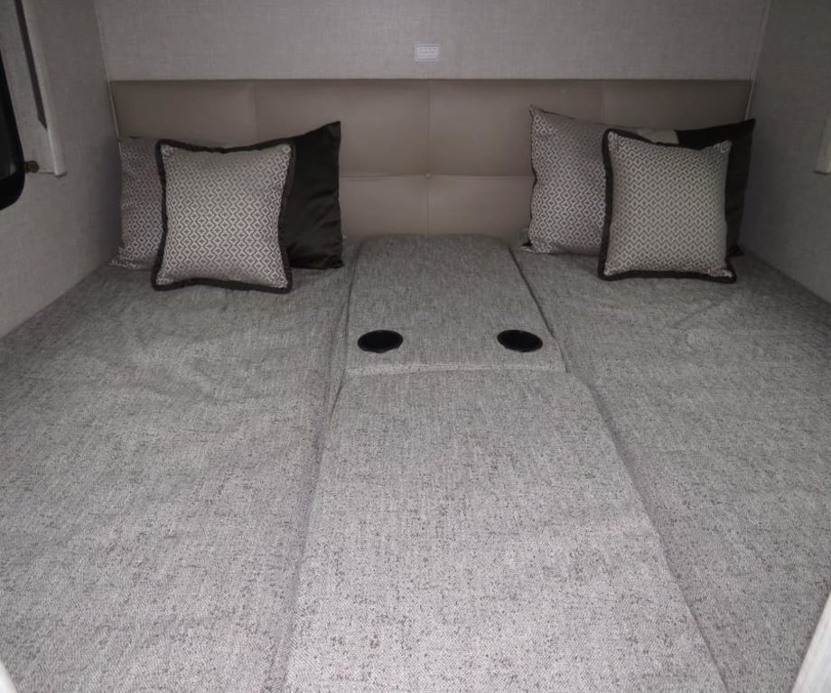 RV rental bedroom: two grey upholstered beds, a beige headboard, and central cupholders, ready for travelers.. Thor Compass 2024
