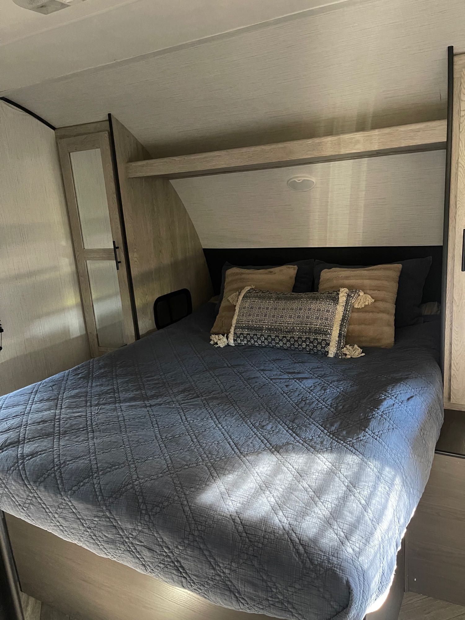 Comfortable RV rental bedroom interior with a blue quilted bed, plush pillows, and modern storage, bathed in sunlight.. Heartland RVs Prowler 2021