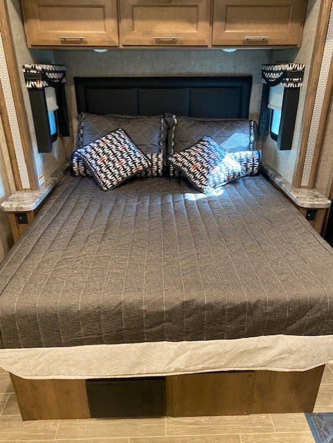 Plush RV rental bedroom with dark bedding, accent pillows, side windows, and overhead storage for comfort.. Thor Outlaw 2022