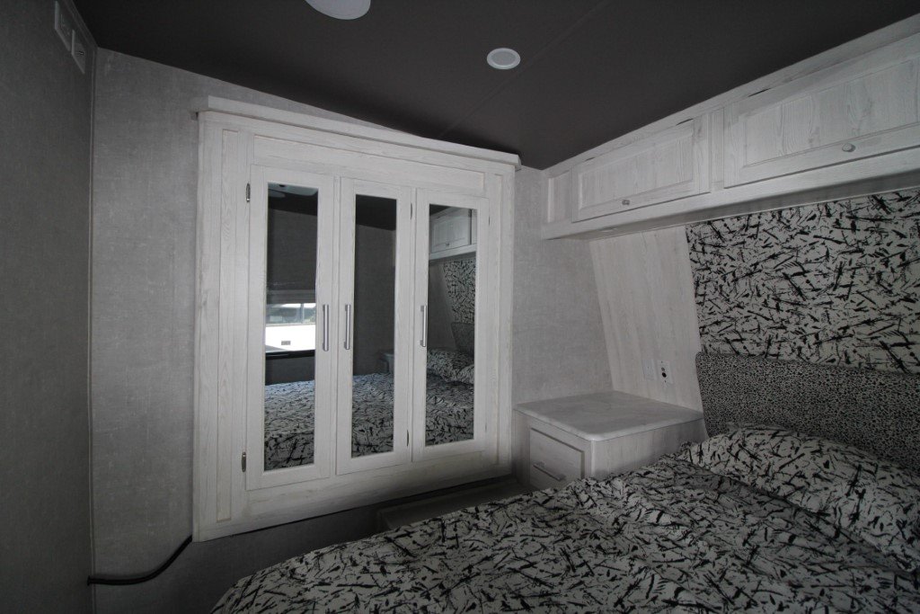 A cozy RV rental bedroom features a bed with a patterned comforter, a mirrored wardrobe, and overhead cabinets.. Eclipse Recreational Vehicles Attitude 2021