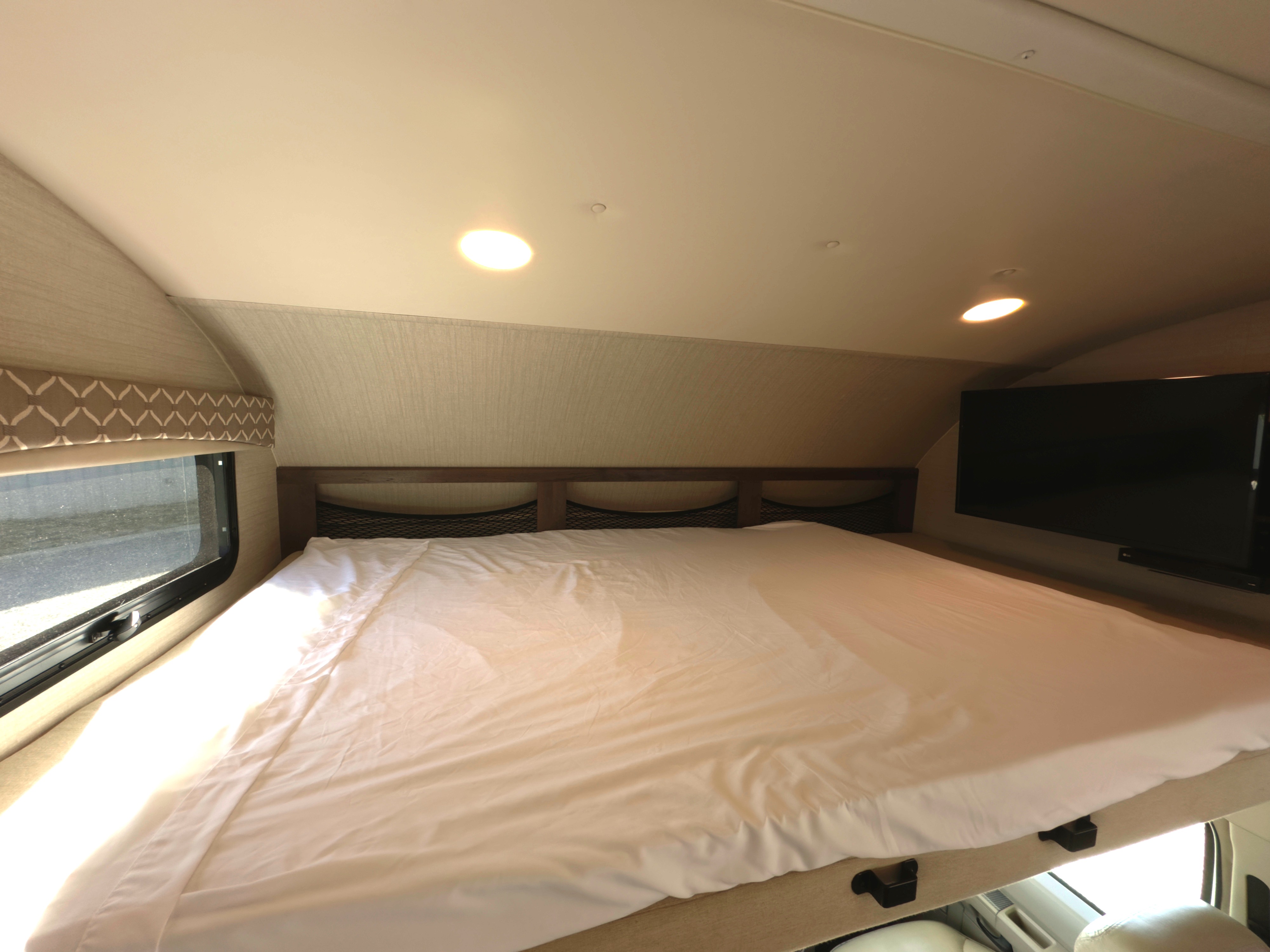 Cozy bed in an RV rental, complete with a window, storage nets, and a TV for comfortable travel.. Jayco Greyhawk 2018