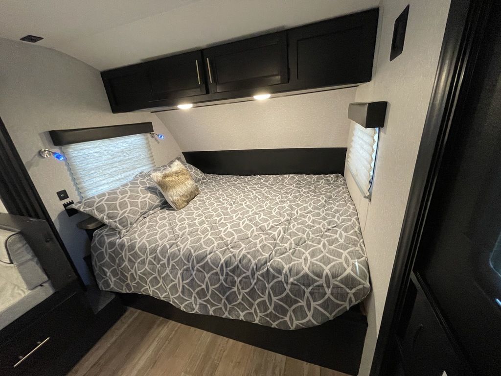 This cozy RV rental bedroom features patterned bedding, overhead storage cabinets, and reading lights for comfortable travel.. Forest River Wolf Pup 2023