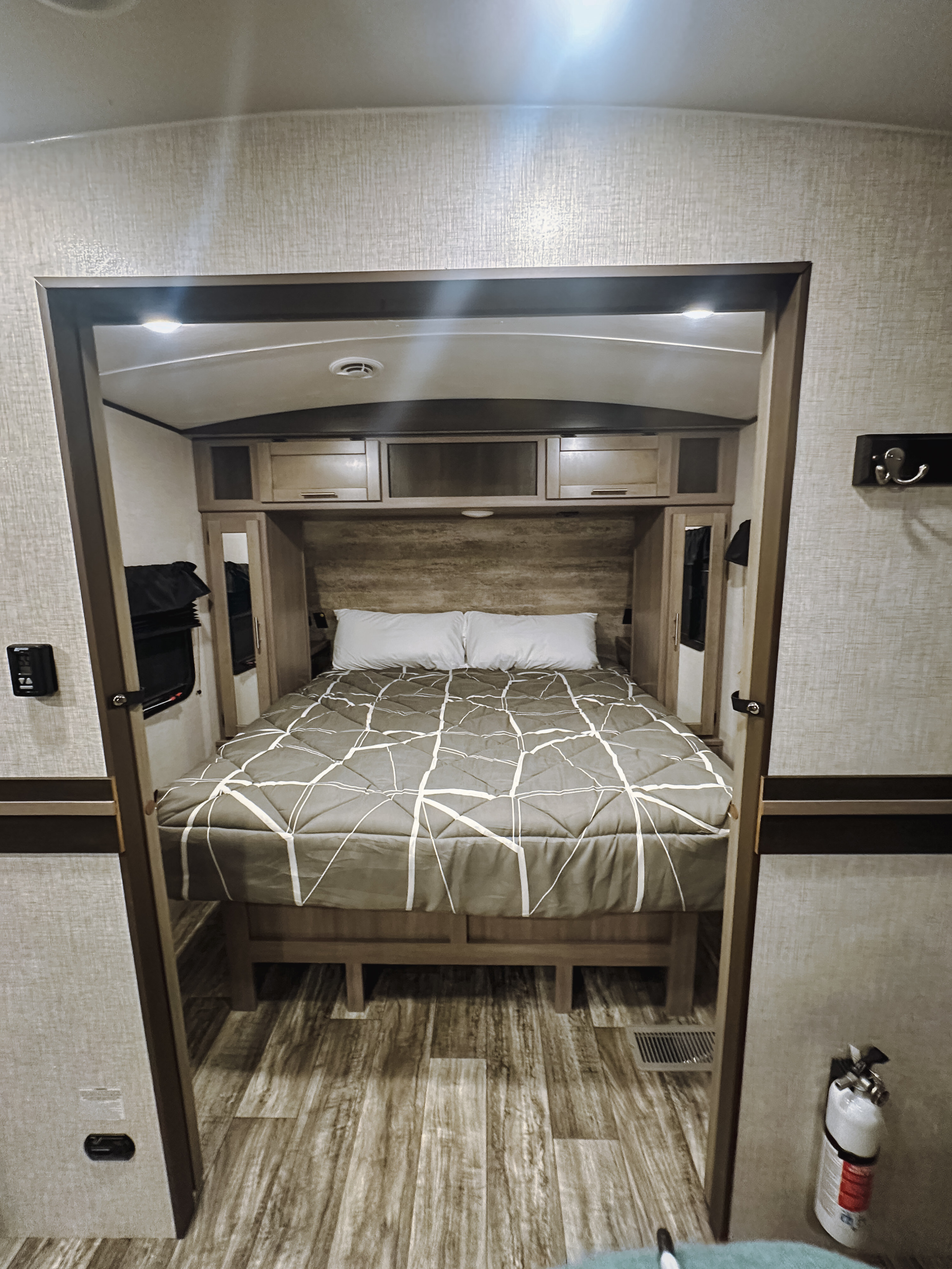 View of an RV rental bedroom through a doorway, showing a compact space with a bed, overhead cabinets, and wood-look floor.. Crossroads RV Sunset Trail Super Lite 2022