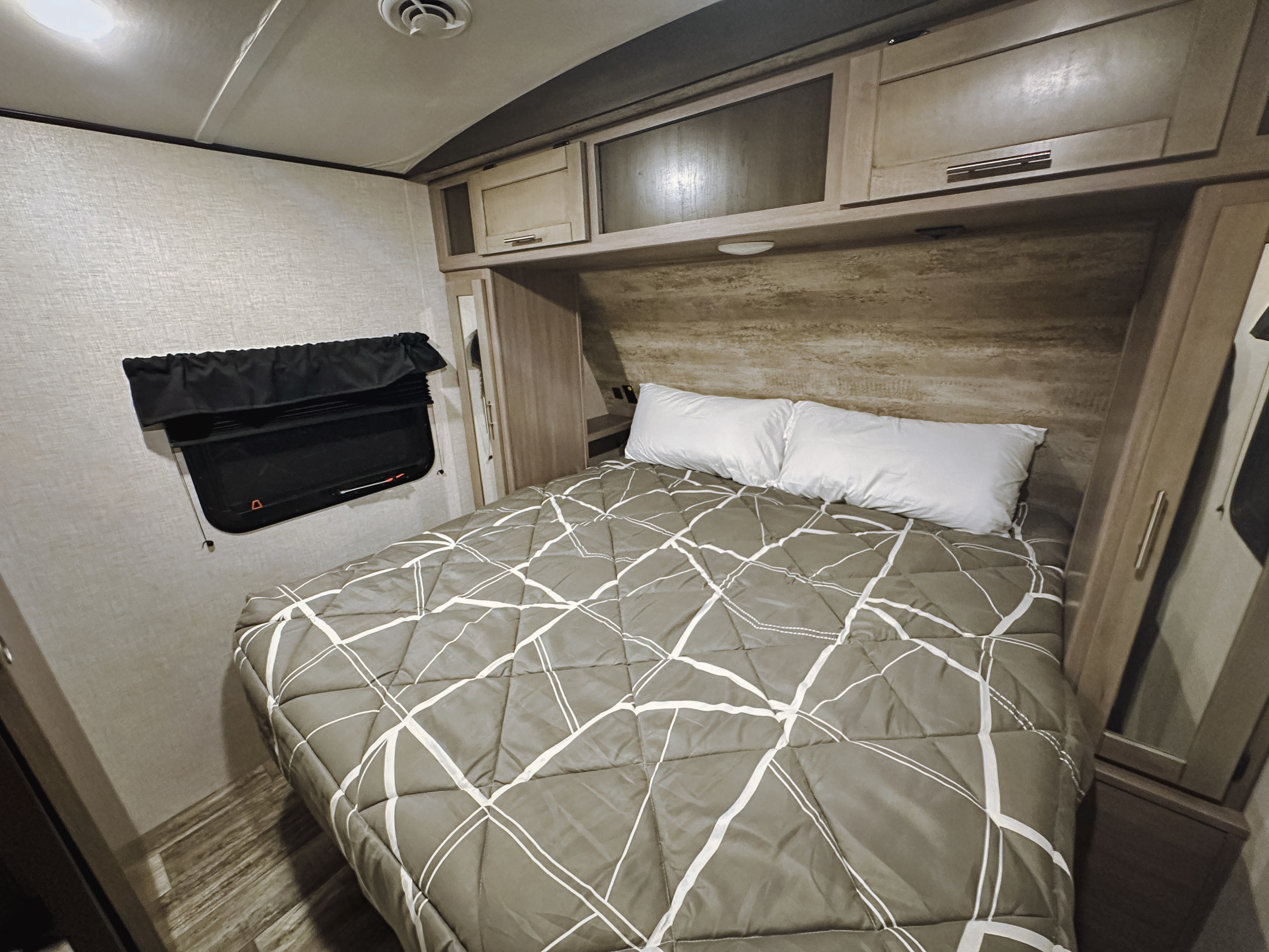 RV rental bedroom: a cozy sleeping area with a bed, white pillows, overhead cabinets, and window with a blackout shade.. Crossroads RV Sunset Trail Super Lite 2022