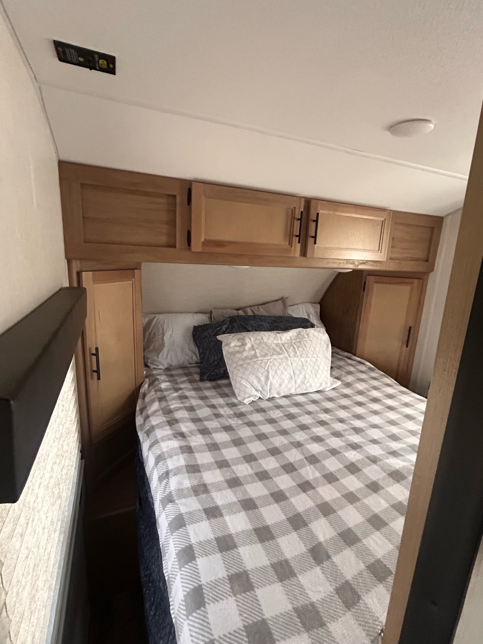 Interior of an RV rental bedroom: bed with grey plaid comforter, wooden overhead storage, and side cabinets.. Forest River Cherokee Wolf Pup 2023