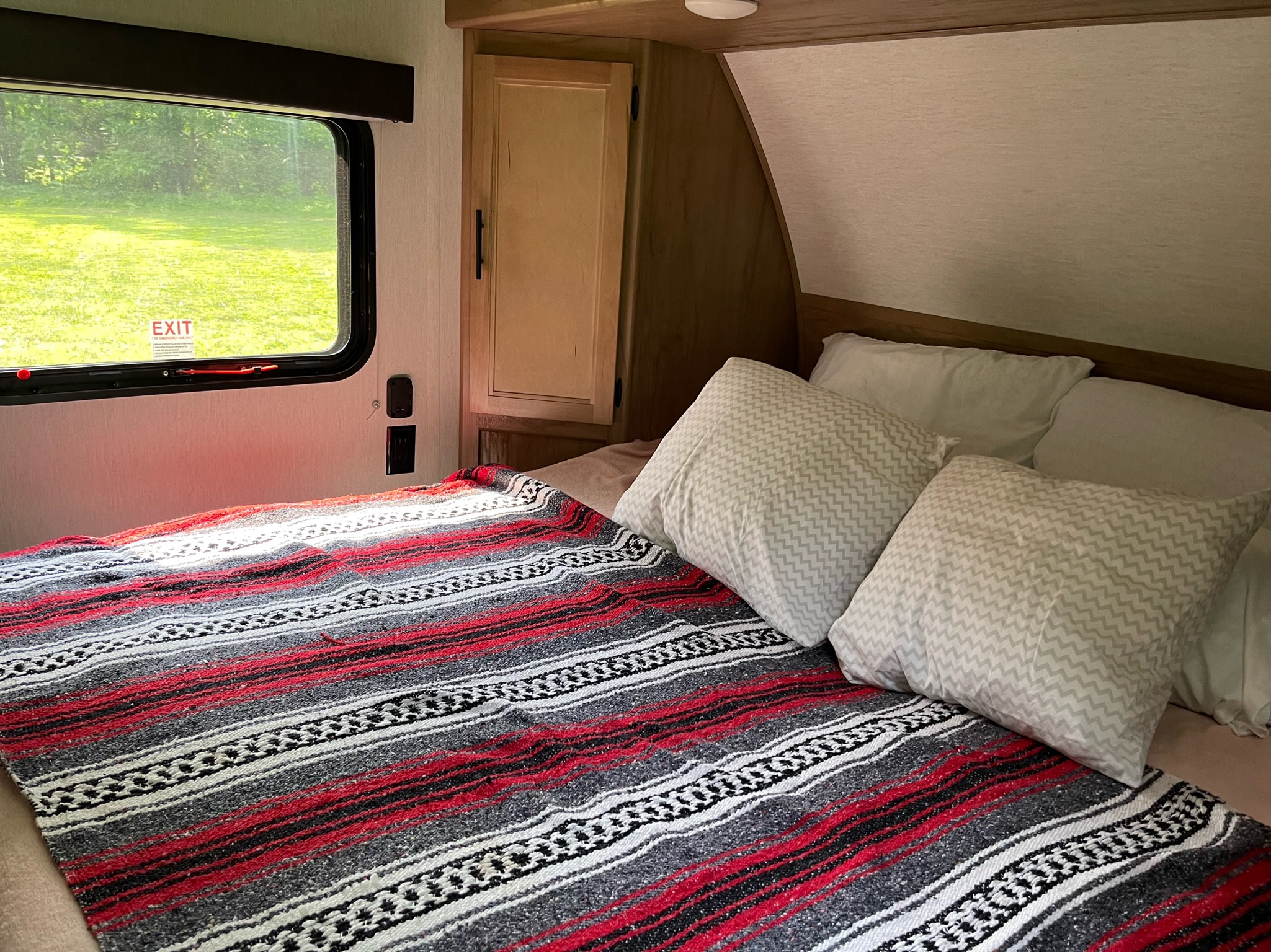 Cozy RV rental interior: bedroom with striped blanket, patterned pillows, and window overlooking green scenery.. Forest River Cherokee Wolf Pup 2023