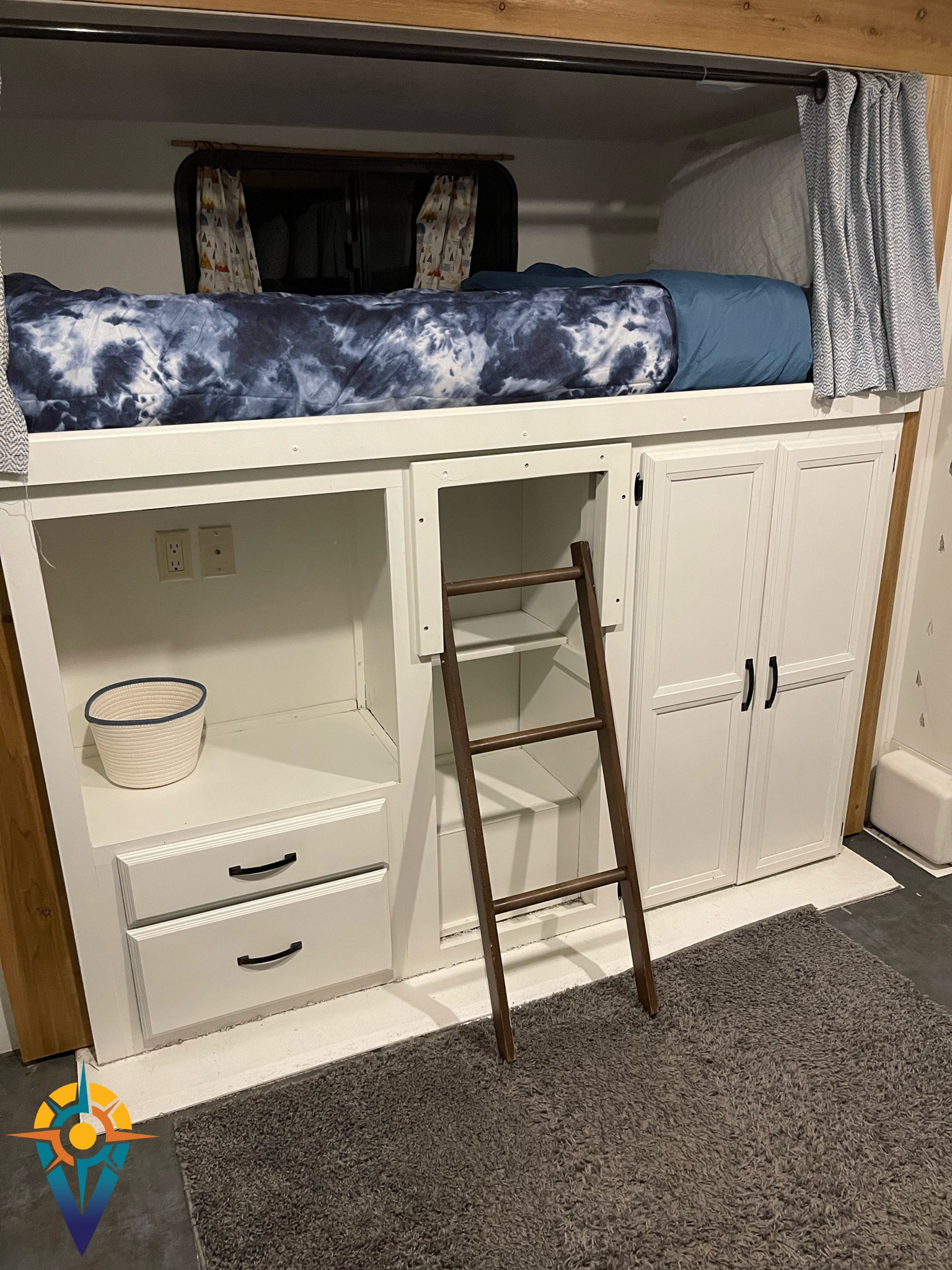 This cozy RV rental features a blue tie-dye bunk bed with white storage, a wooden ladder, and a soft grey rug.. Forest River Wildwood DLX 402QBQ