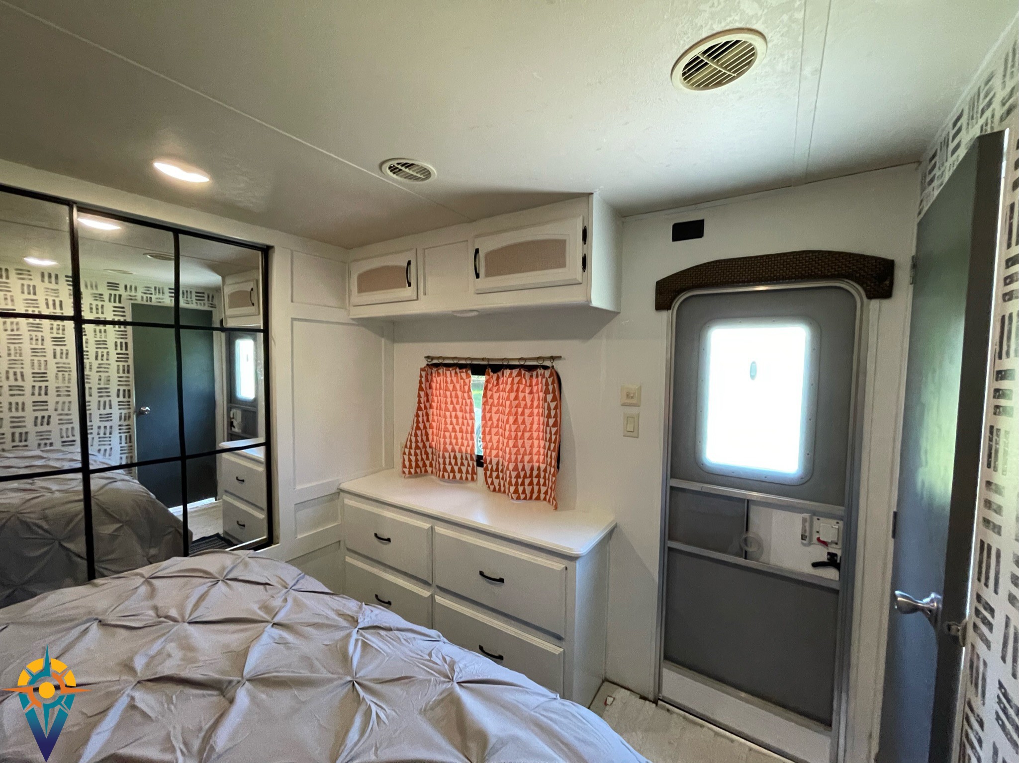 Cozy RV rental bedroom interior with a comfortable bed, mirrored closet, built-in dresser, and an exterior door.. Forest River Wildwood DLX 402QBQ