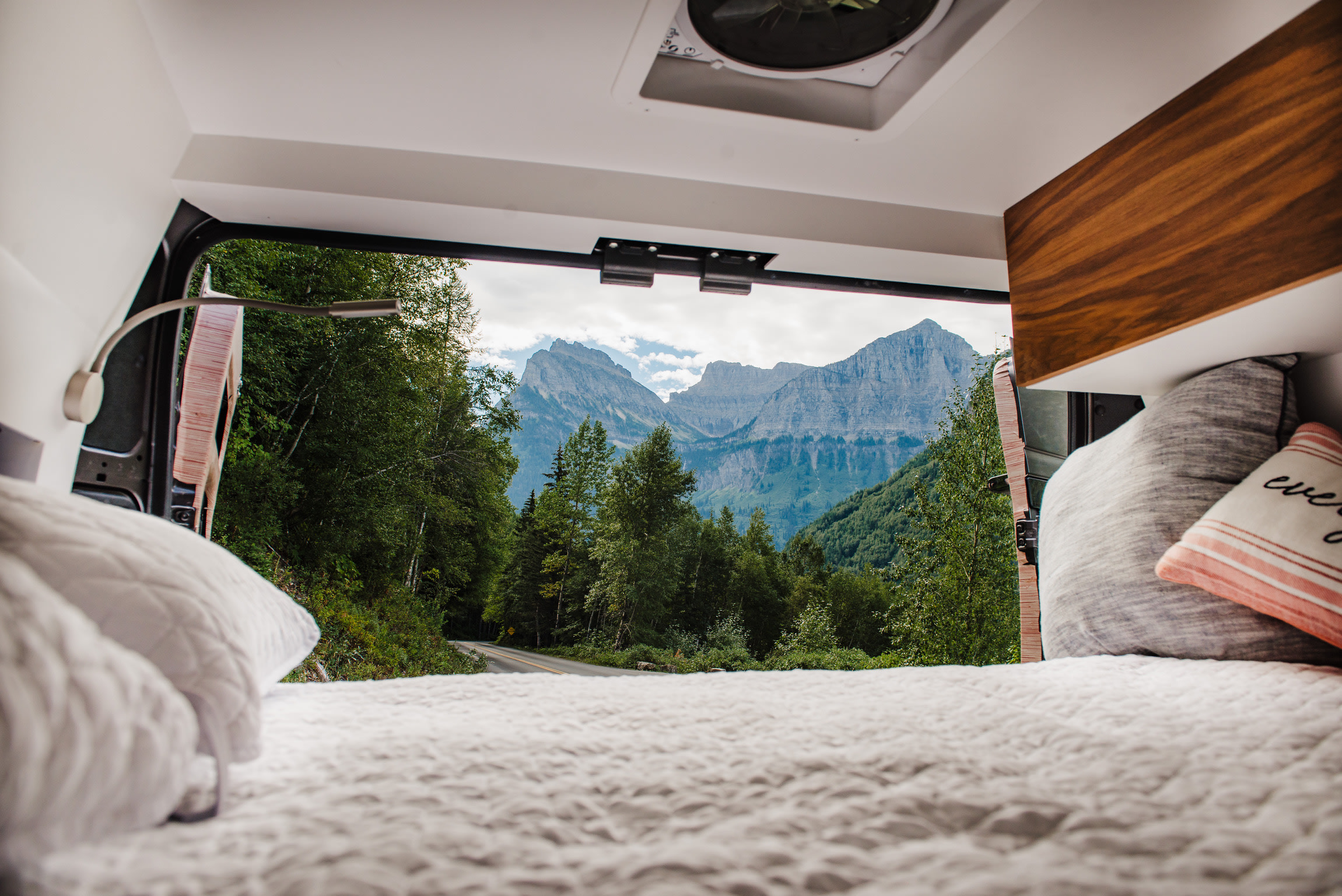 RV rental bed offers a cozy interior view of a scenic mountain road, lush forest, and grand peaks.. RAM Promaster 3500 2021