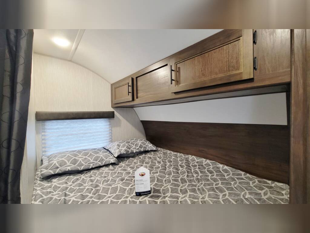 Cozy RV rental bedroom with patterned bedding, overhead cabinets, and window blinds. Ideal for comfortable travel.. Forest River Cherokee Grey Wolf 2020