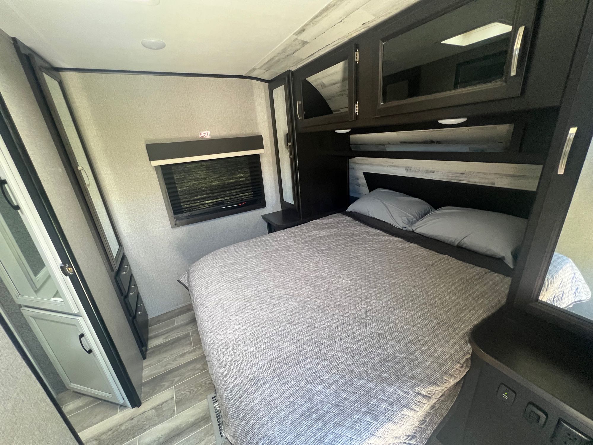 Modern RV rental bedroom interior with cozy bed, stylish dark cabinetry, and wood-look flooring for a compact stay.. Jayco Jay Feather 2021