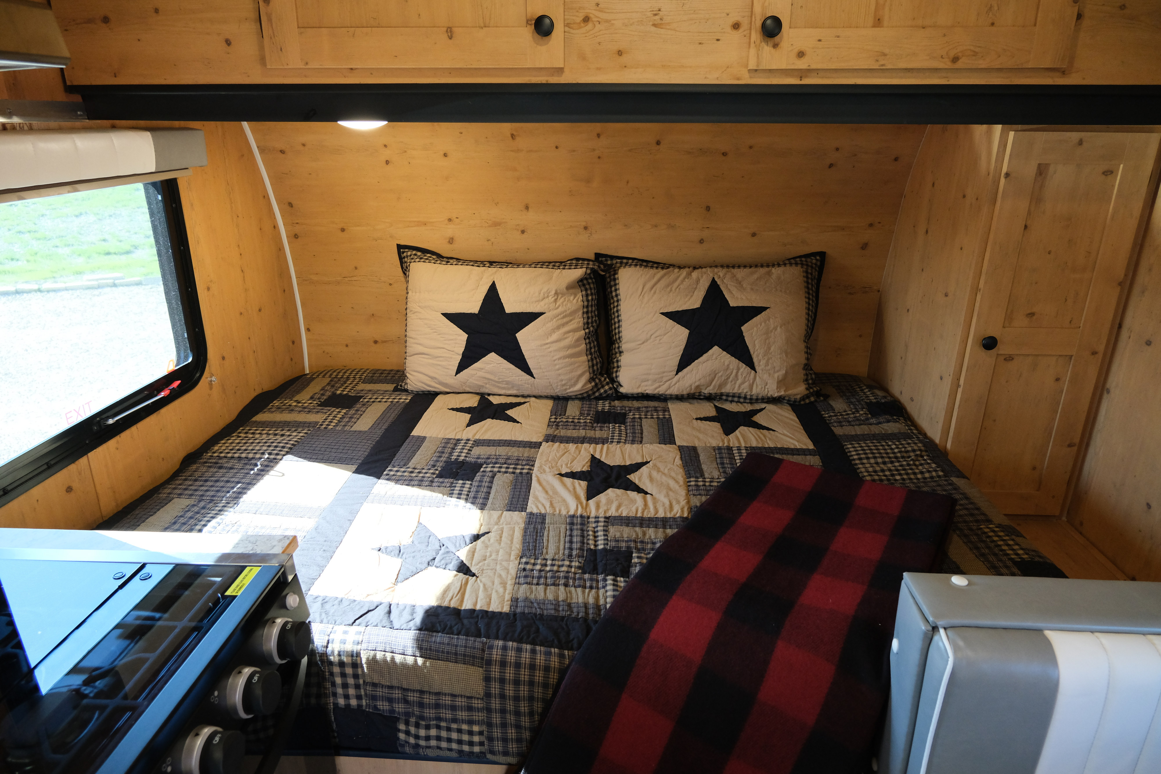 Inside a cozy **rv rental** featuring a bed with star-patterned quilt, wooden walls, and a compact stove.. Sunray Sunlite 16BH 2023