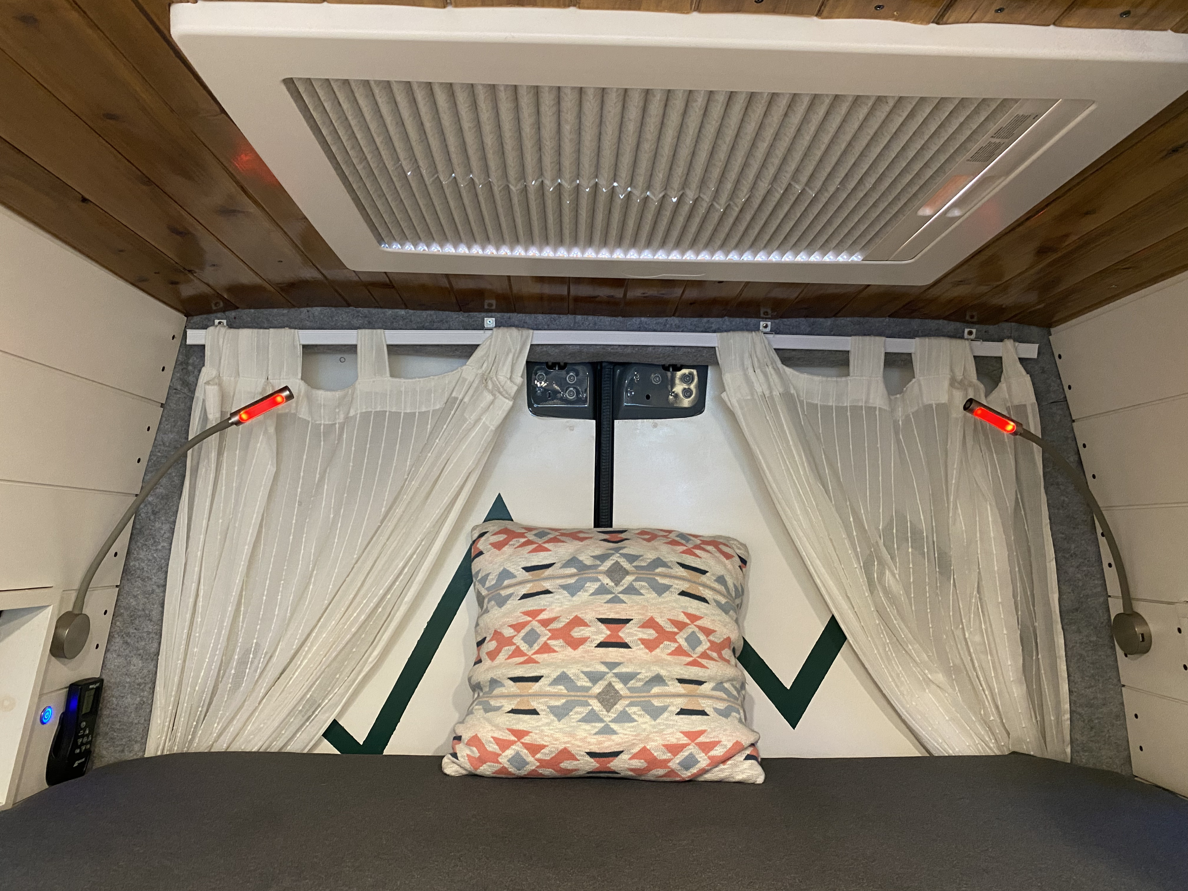 Cozy RV rental bedroom featuring a comfortable bed with reading lights, white privacy curtains, and an overhead fan/vent.. Mercedes Sprinter Premium 2020
