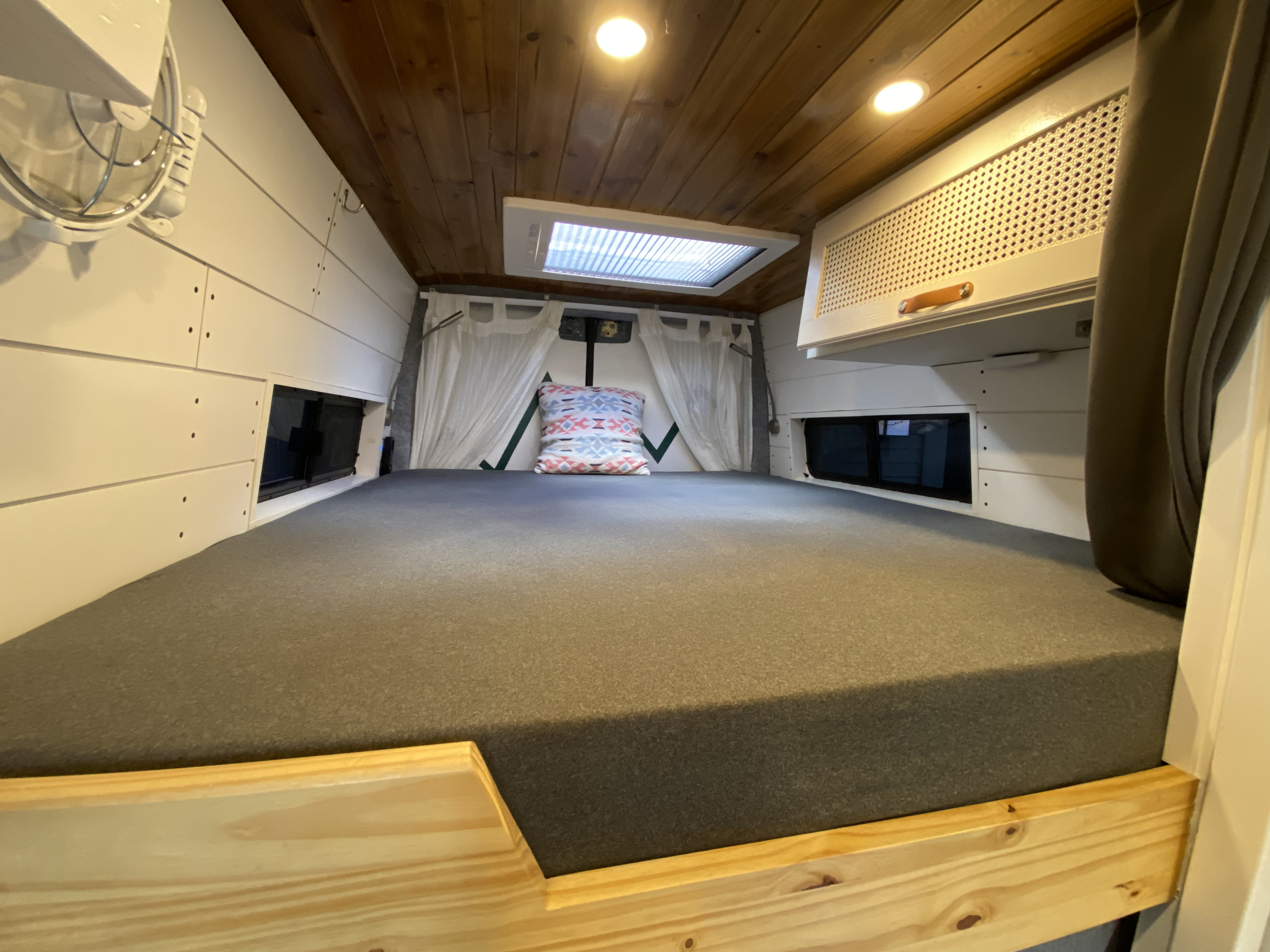 Interior of an RV rental showing a large, comfortable bed, skylight, and overhead cabinet.. Mercedes Sprinter Premium 2020