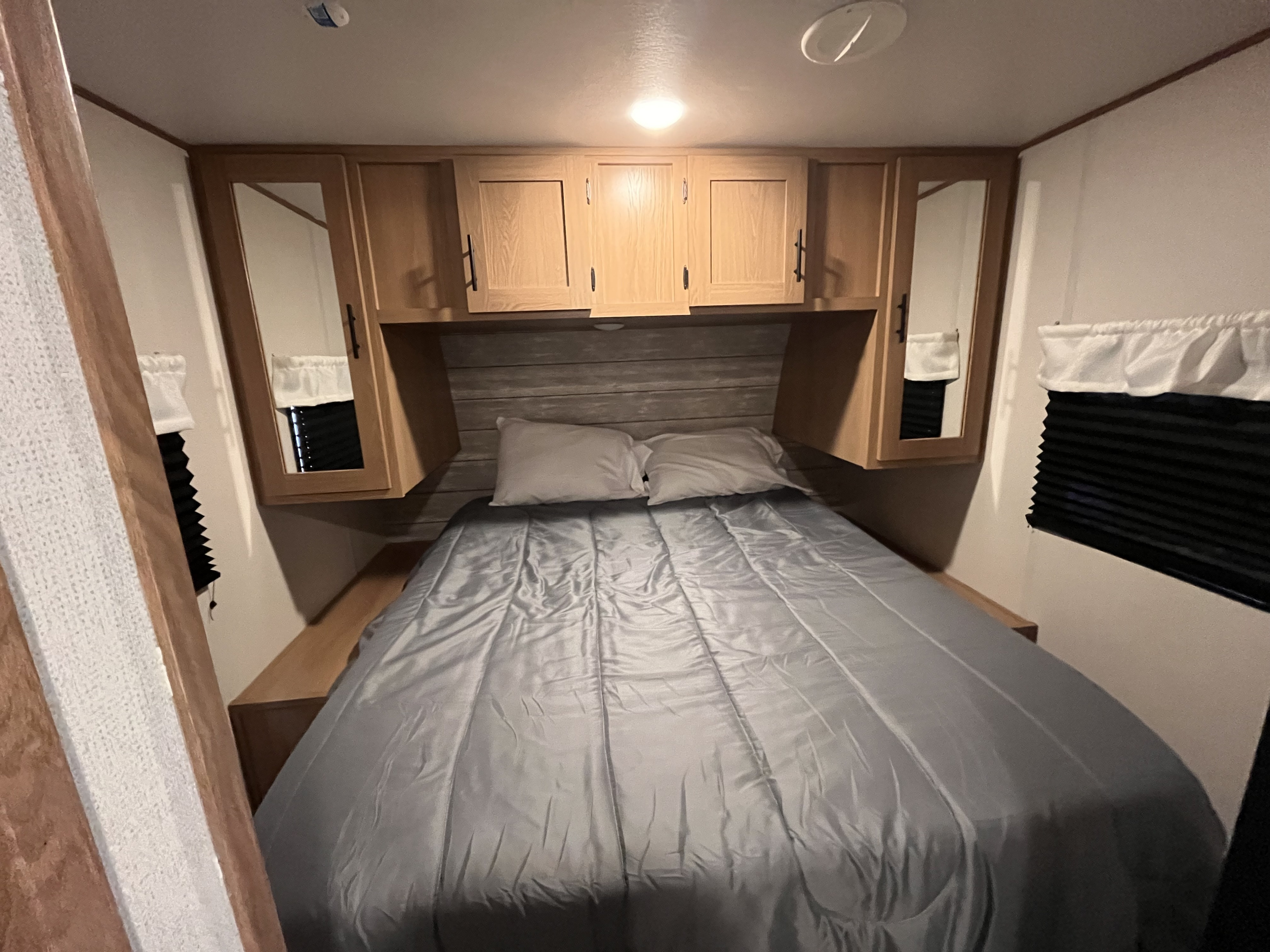 Cozy RV rental bedroom with a comfortable bed, wood cabinets, and window blinds. Ideal for travel.. Forest River Prime Time Avenger 27 DBS 2023