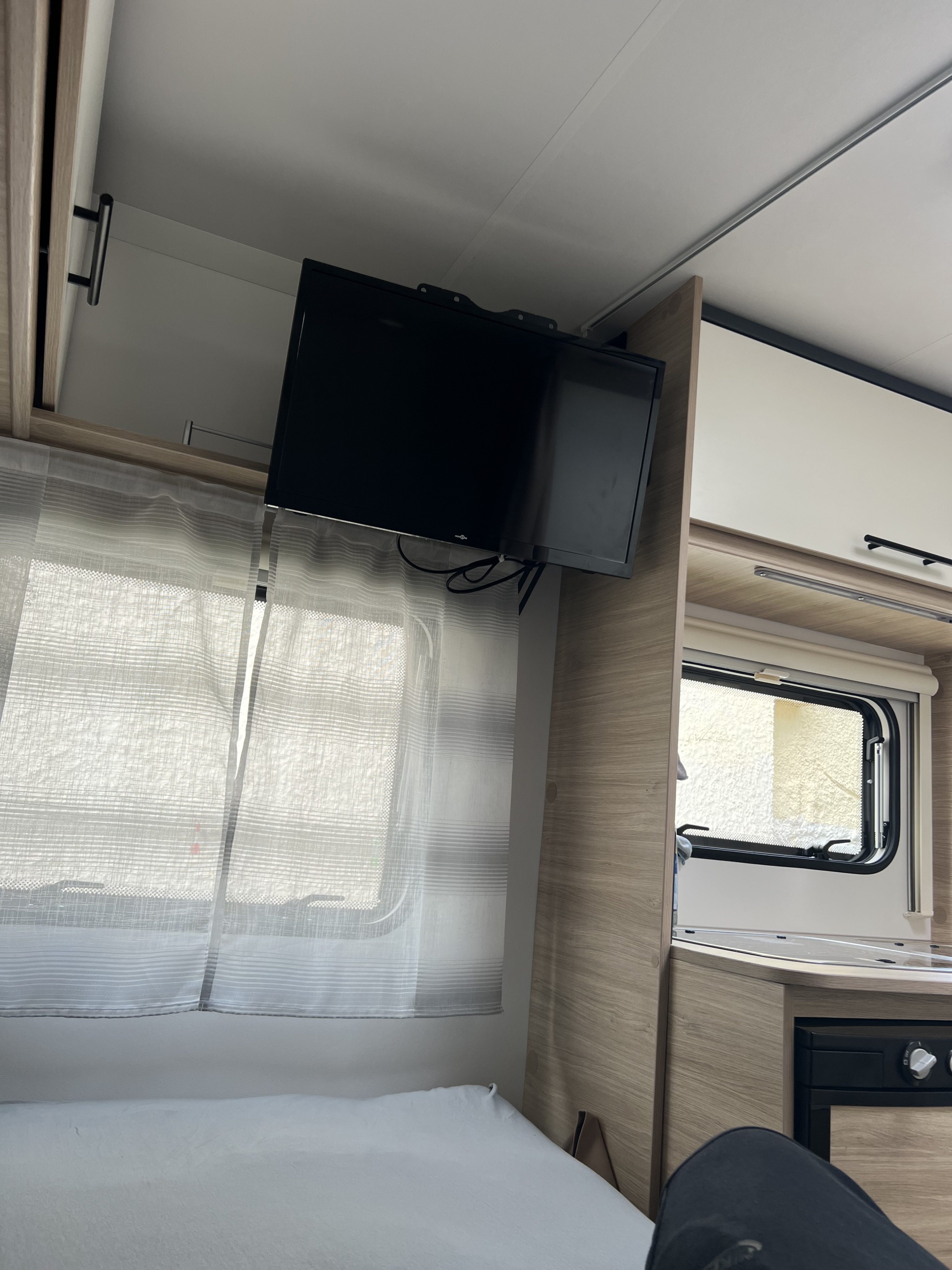 Cozy rv rental interior featuring a mounted TV above the bed, a window with curtains, and a compact kitchenette.. Sterckeman 390 CP 2023