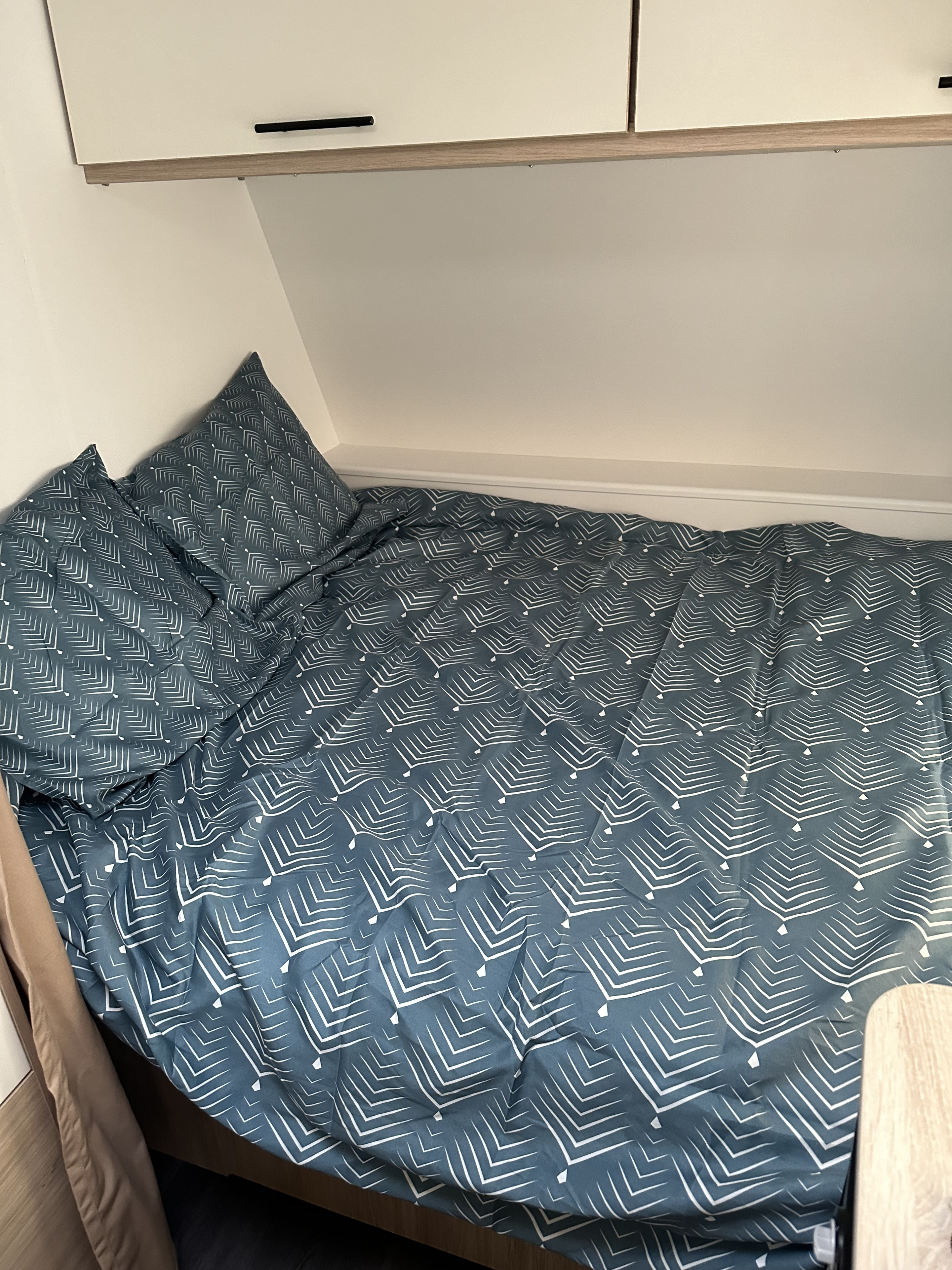 A cozy RV rental bed featuring teal patterned bedding, pillows, and overhead storage cabinets.. Sterckeman 390 CP 2023
